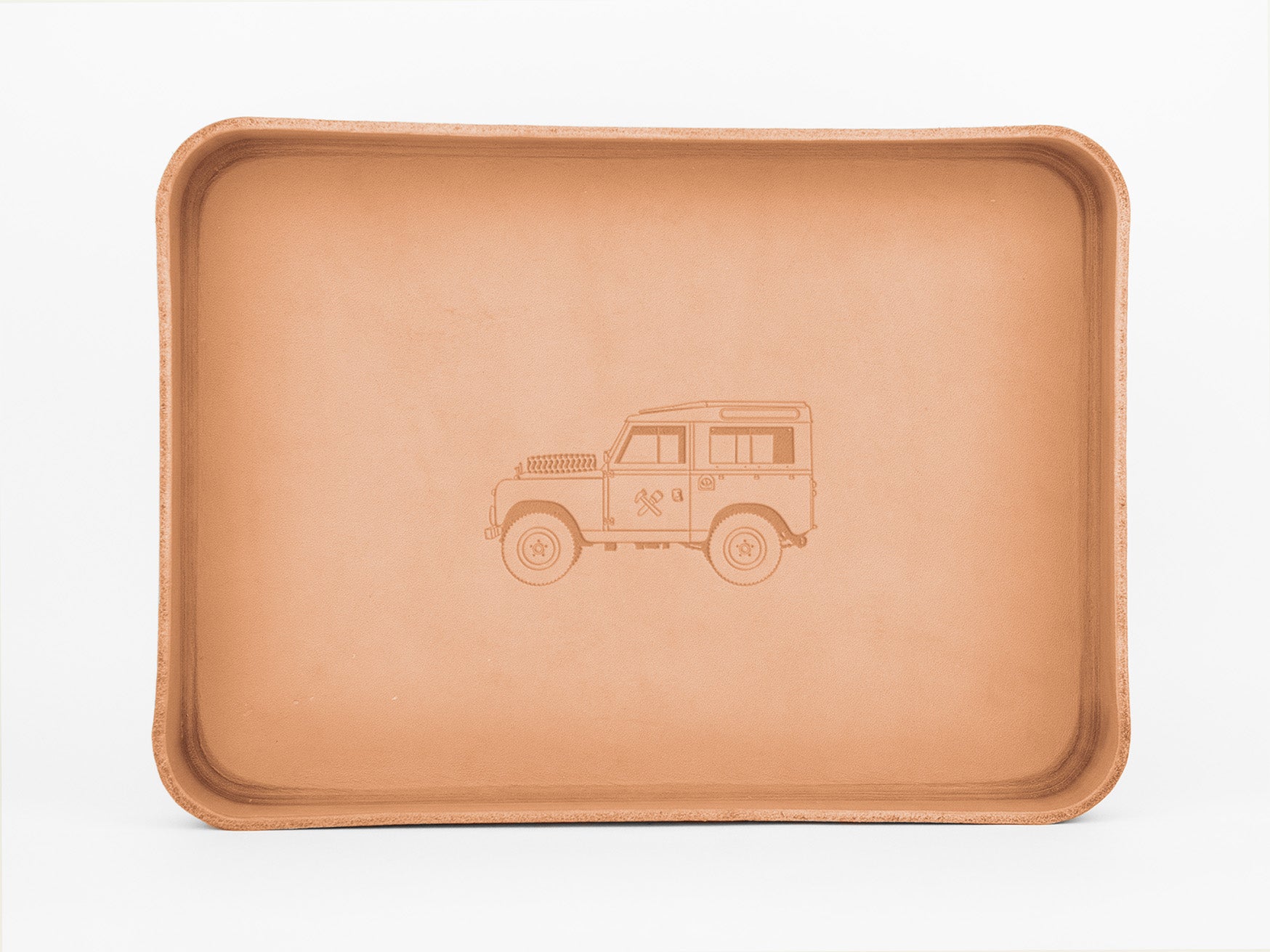 A rectangular tan leather tray featuring an embossed outline of a classic off-road vehicle, resembling a vintage Land Rover, centered on the base. The tray has raised edges and a smooth finish.