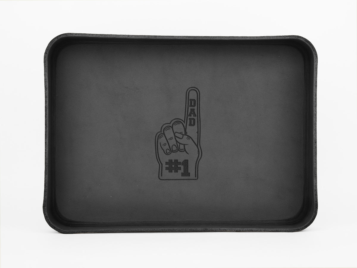 A rectangular black tray with an illustration of a foam finger in the center, labeled DAD on the finger and #1 at the base. The background of the tray is plain and unadorned.