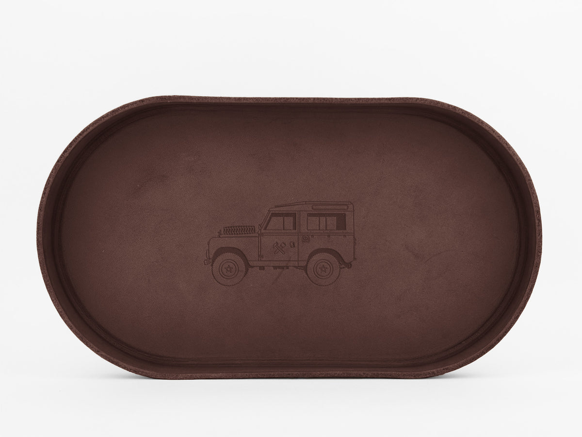 A brown, oval-shaped tray with an engraved illustration of a classic off-road vehicle, similar to a Land Rover, centered on the bottom surface. The background is plain white.

