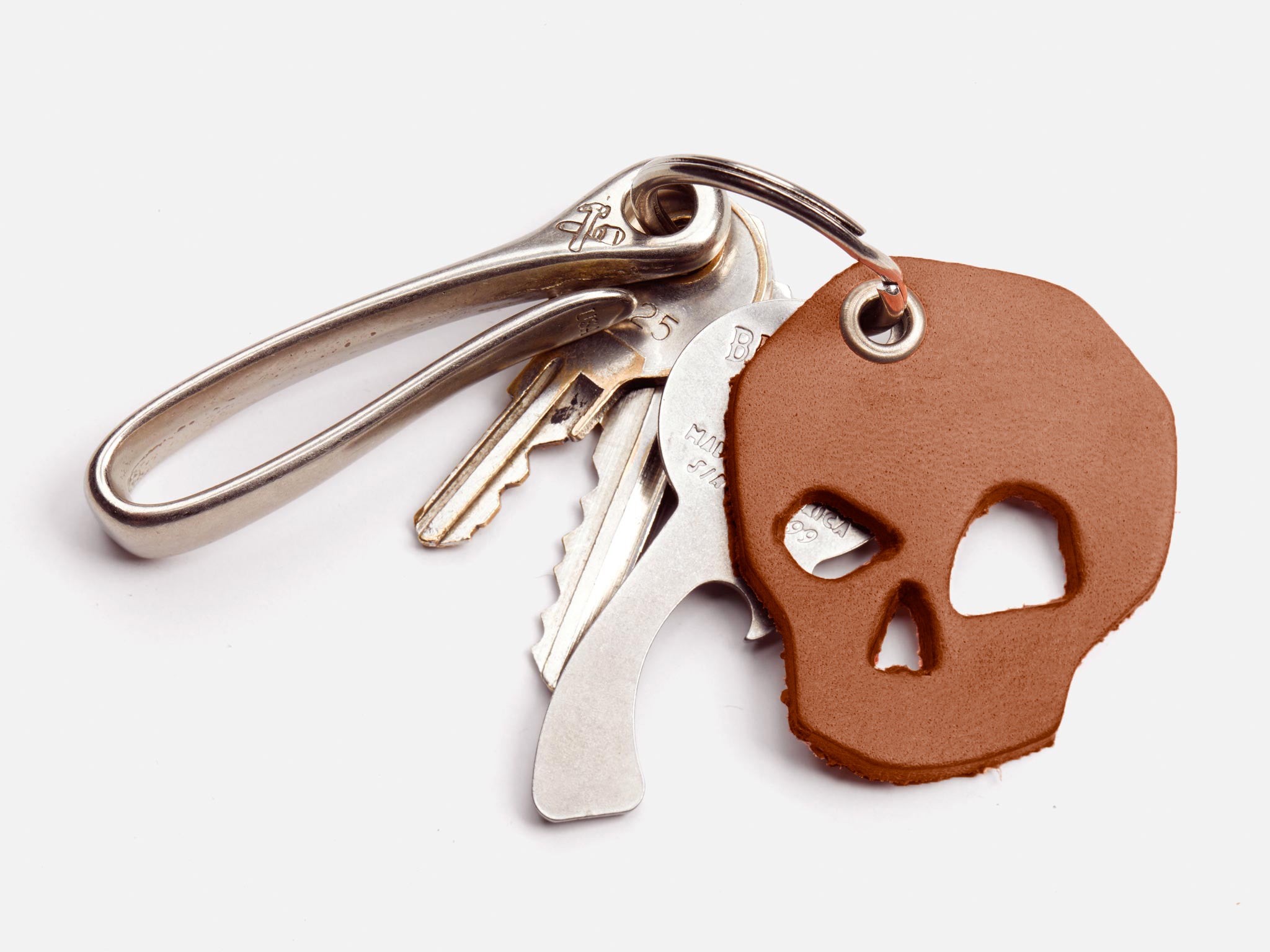 A set of keys on a metal keyring with a brown leather keychain shaped like a skull, against a white background.