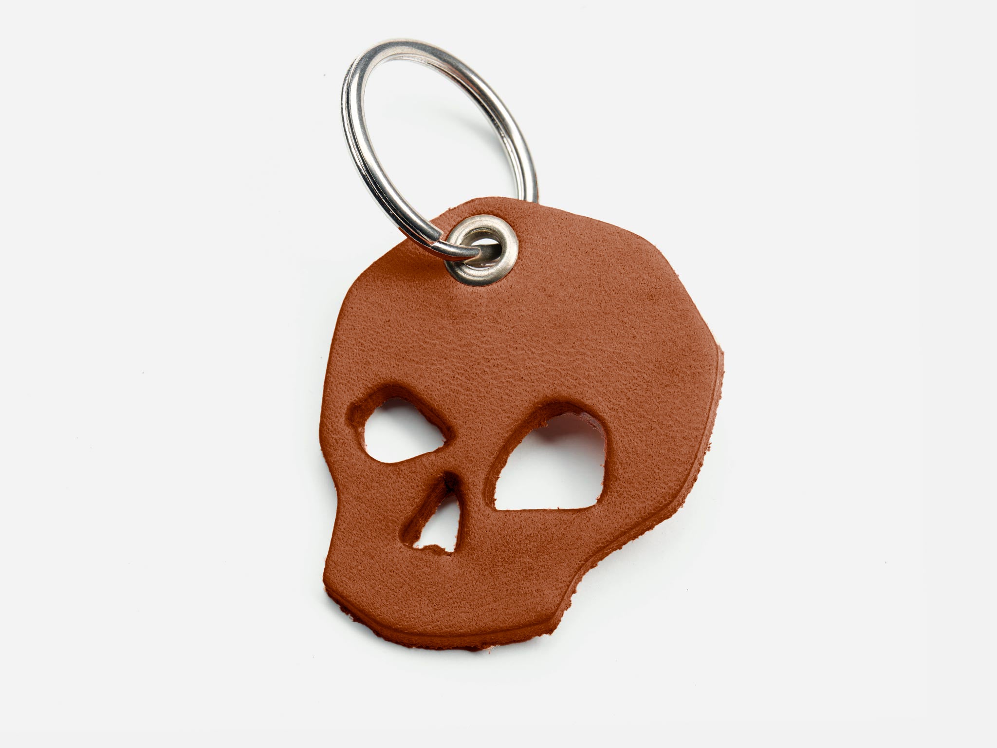A brown leather keychain in the shape of a skull with cut-out eyes and nose, attached to a silver metal keyring, on a white background.