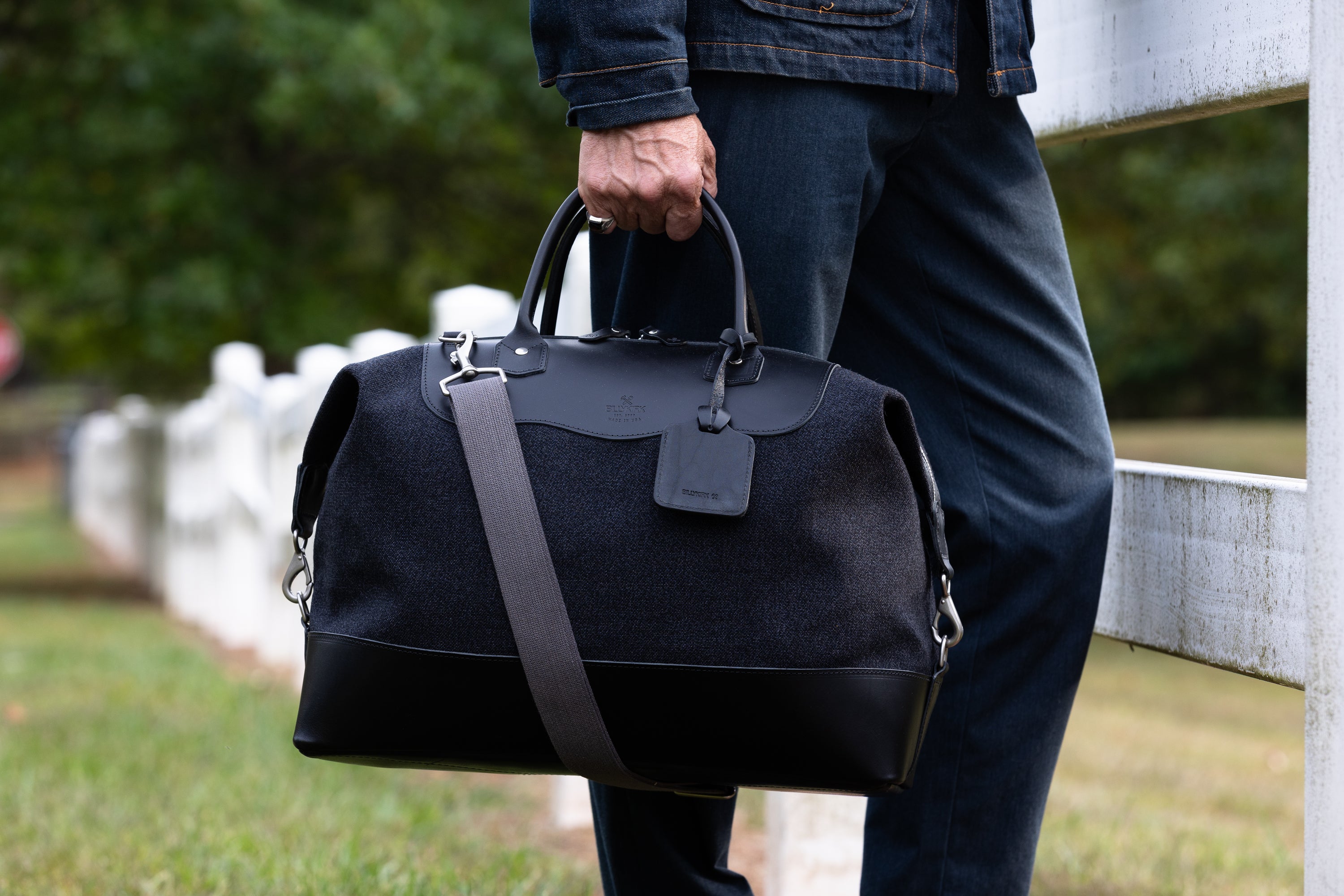Person holding a black carryall bag outdoors with a blurred background