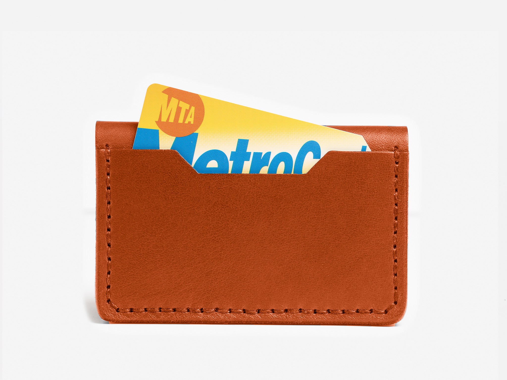 A brown leather card holder with a New York MTA MetroCard partially visible inside against a plain white background.