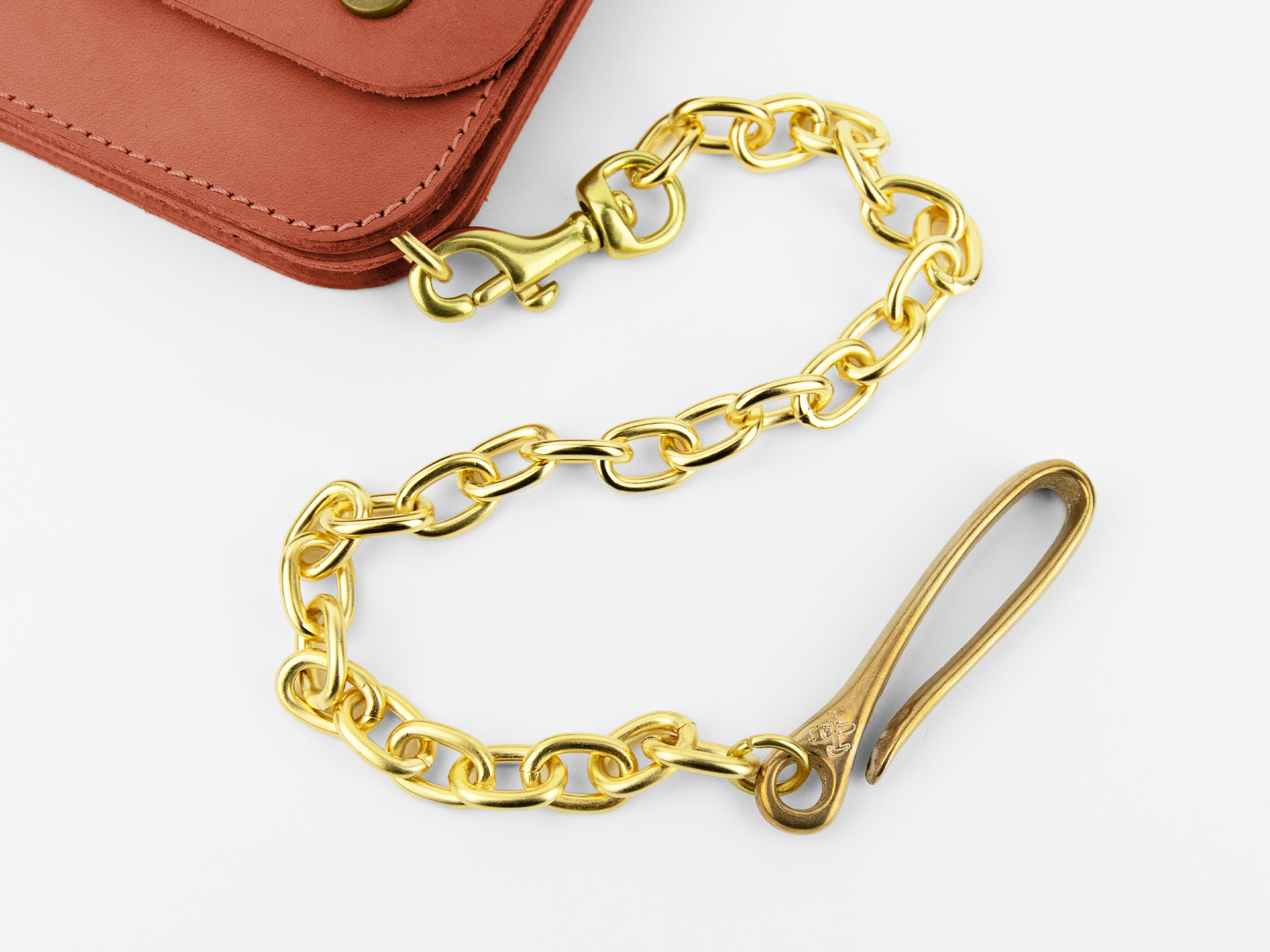 A close-up of a gold chain with a hook on one end and a clasp on the other, attached to the corner of a brown leather wallet on a white background.