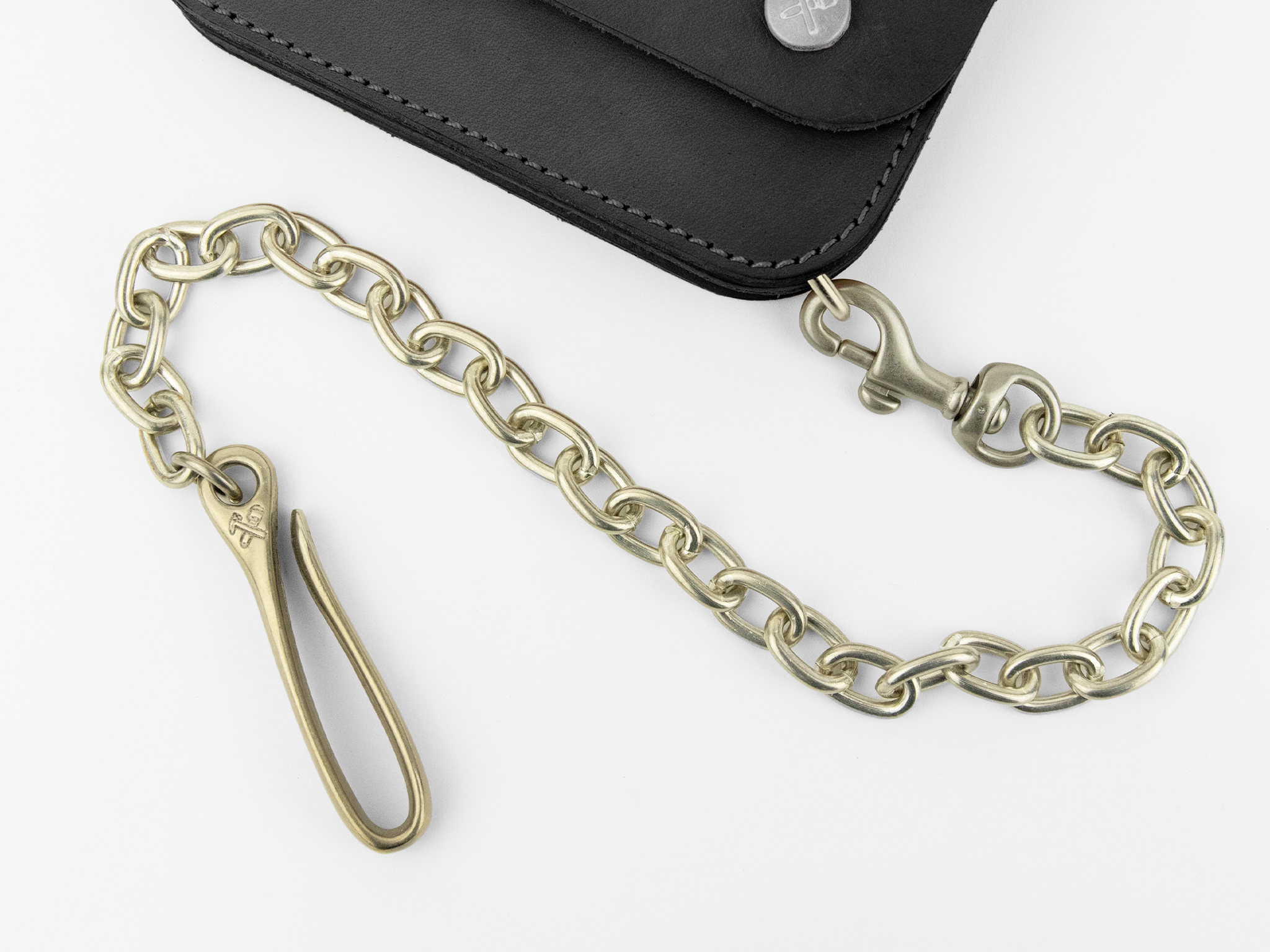A brass chain with a hook and clasp is attached to a black leather wallet positioned in the top corner against a white background.