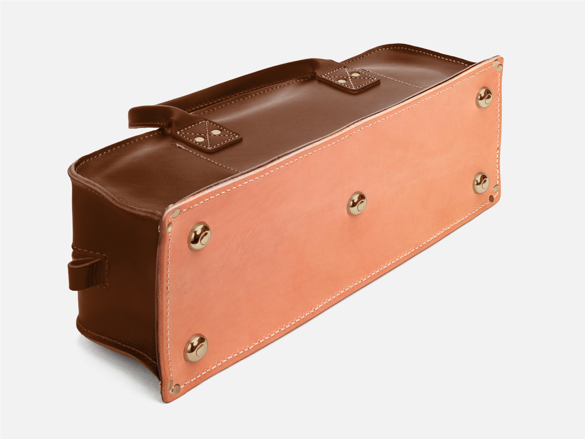 A brown leather bag shown from the bottom, featuring a light tan leather base with four metal feet and visible white stitching along the edges.