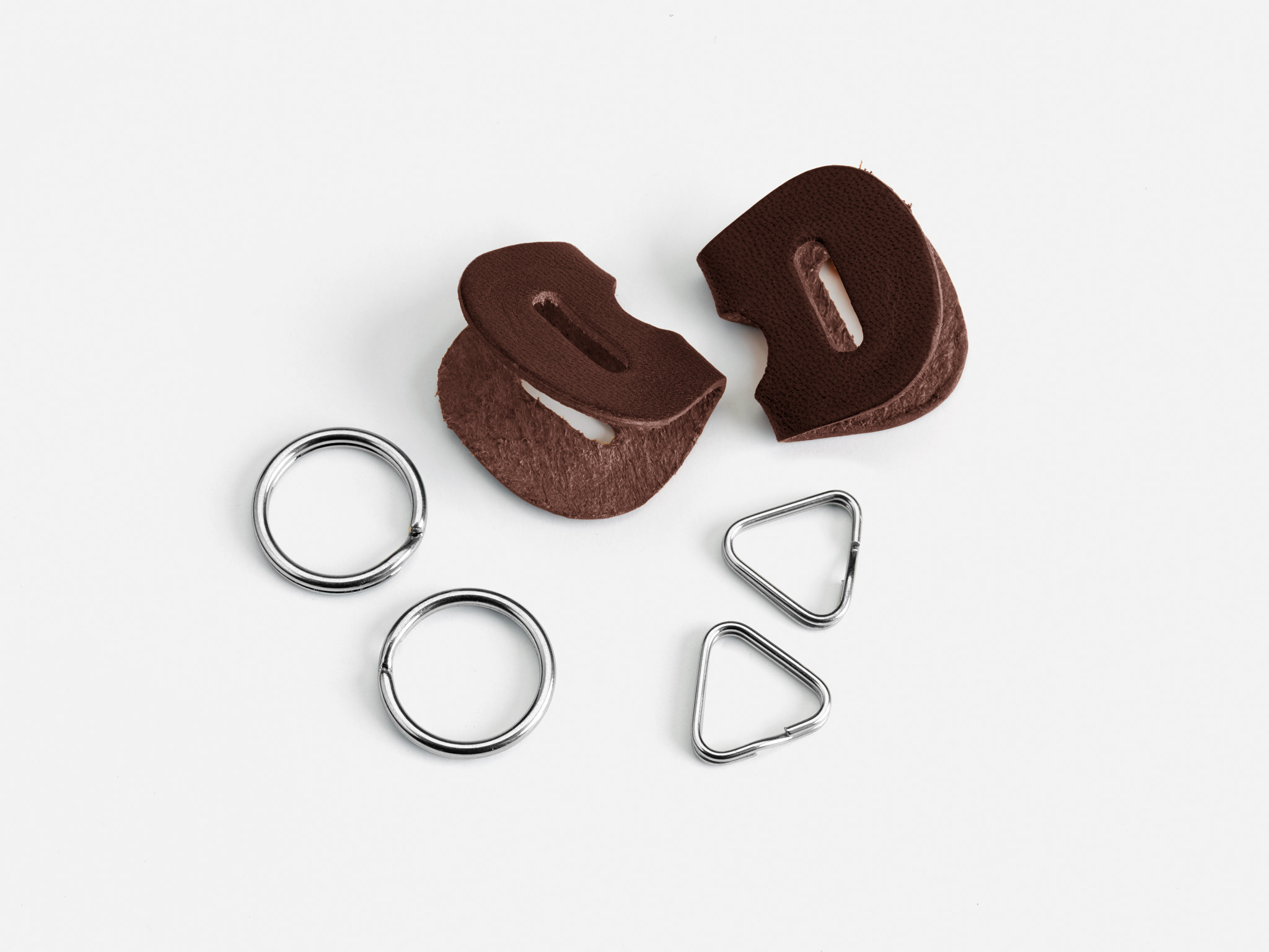 Two brown leather pieces with slits, two round metal rings, and two triangular metal rings are arranged on a white background.