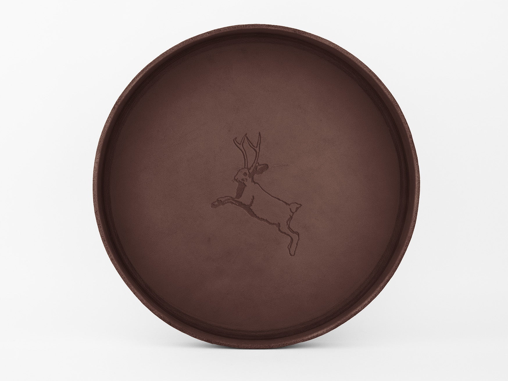 	
A round, brown leather tray with an embossed outline of a leaping jackrabbit with antlers (a jackalope) in the center, set against a plain white background.