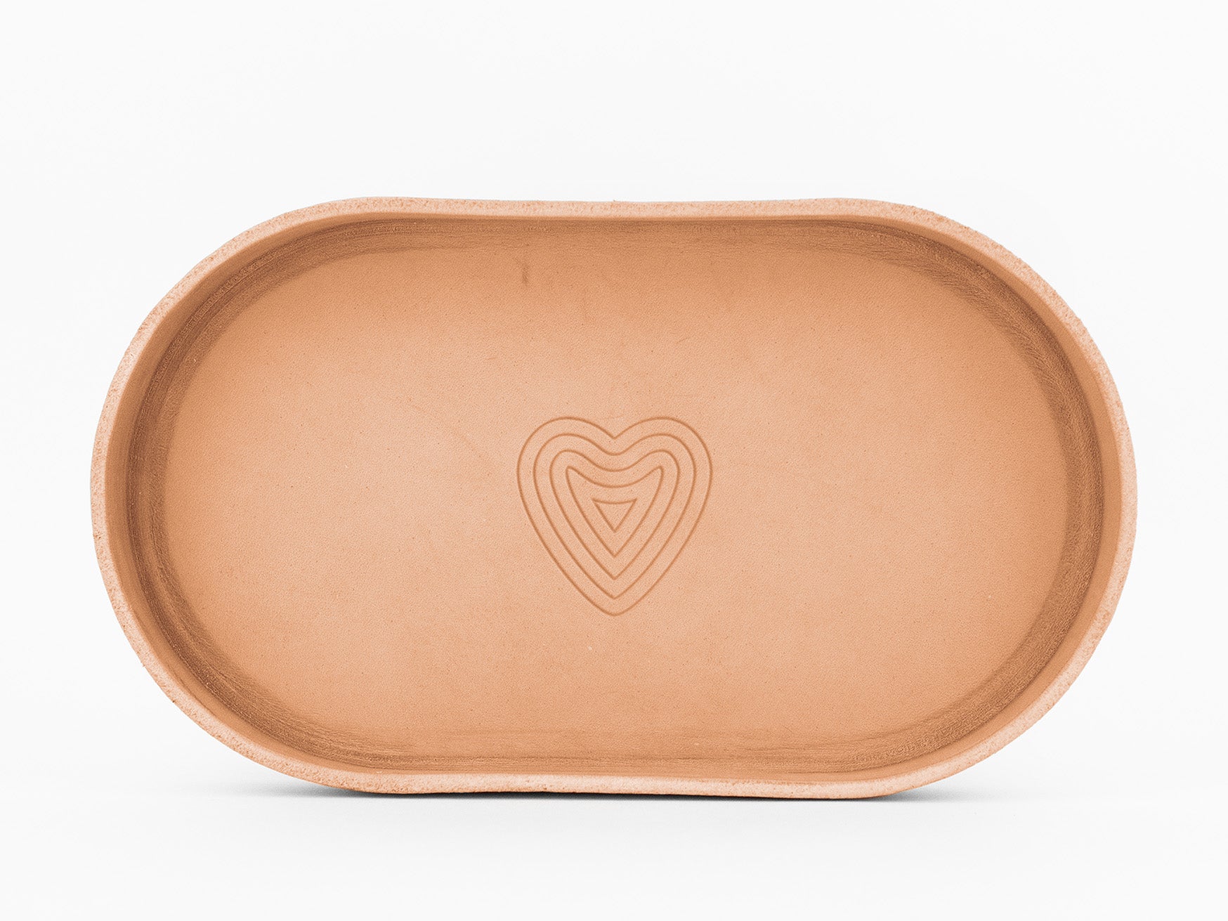 A simple, oval-shaped, natural colored  tray with debossed heart design in the center, photographed on a white background.