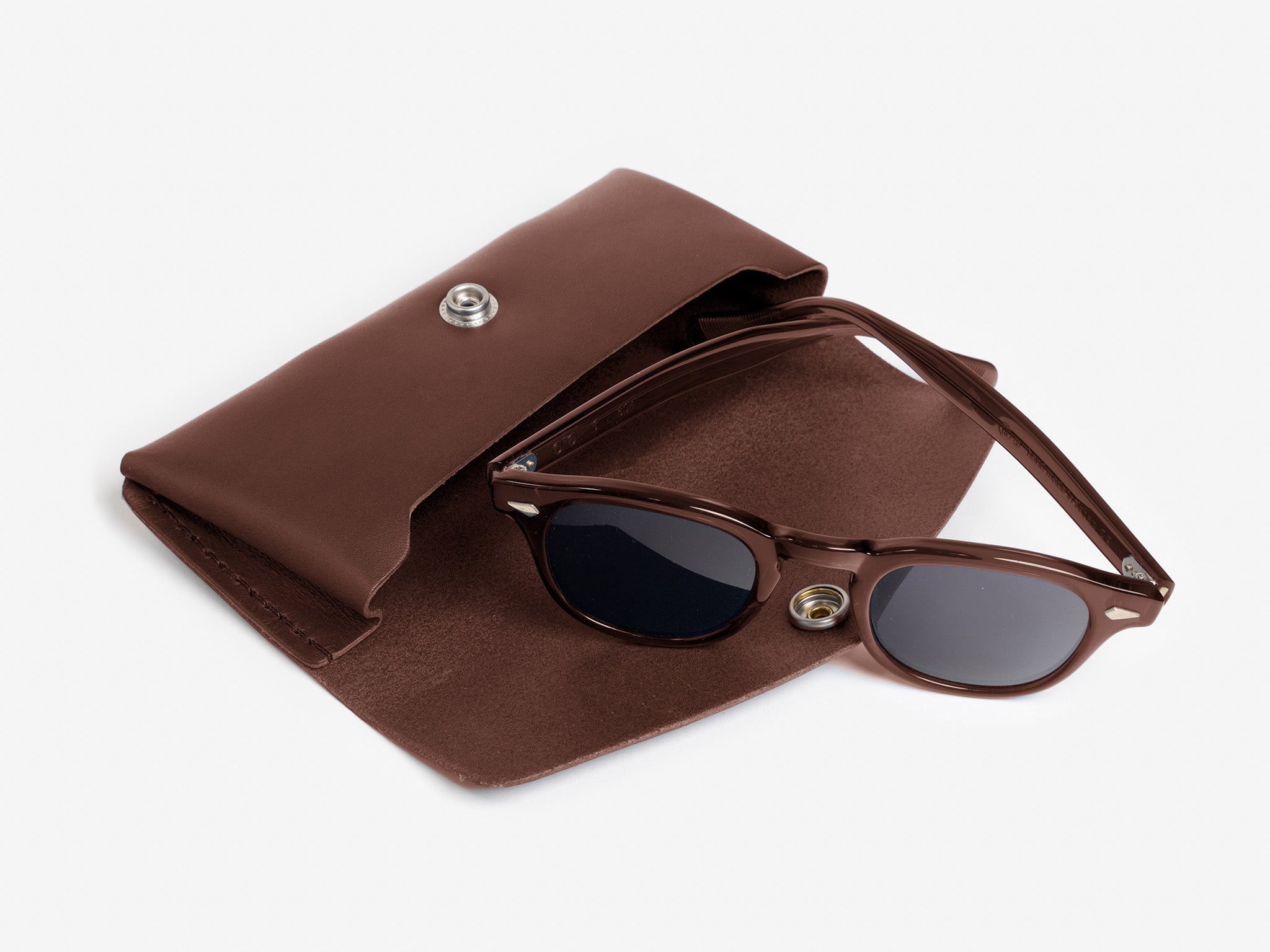 Brown sunglasses with dark lenses rest on an open brown leather case with a snap button, all set against a white background.