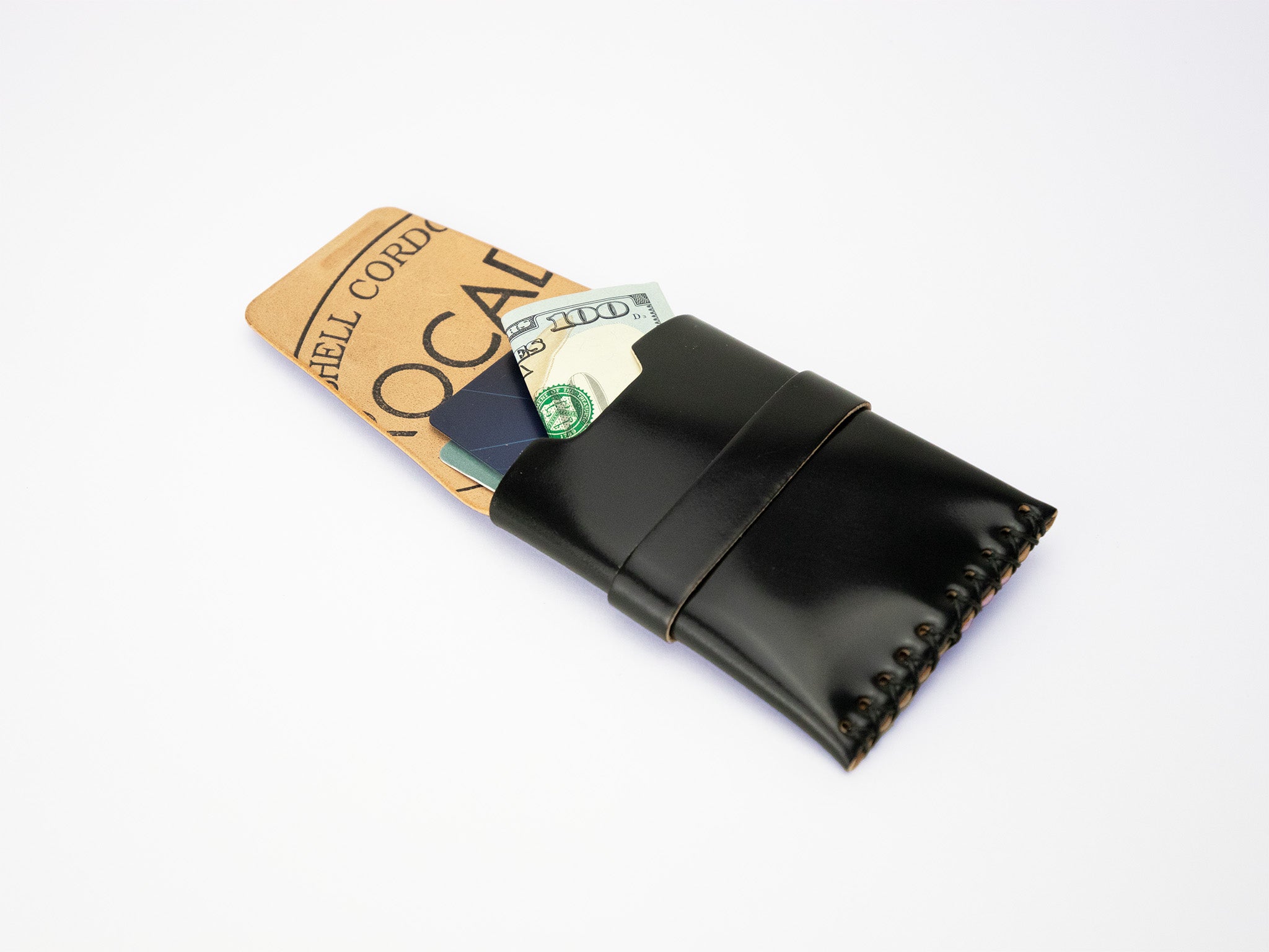 A black leather wallet with visible stitching holds a folded hundred-dollar bill and a brown card, all placed on a plain white background.