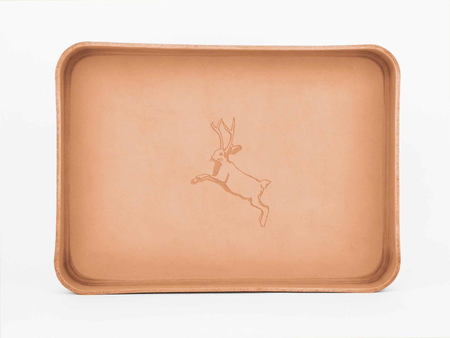 A rectangular tan leather tray with raised edges, featuring an engraved outline of a leaping jackalope (a rabbit with antlers) in the center. The background is plain white.