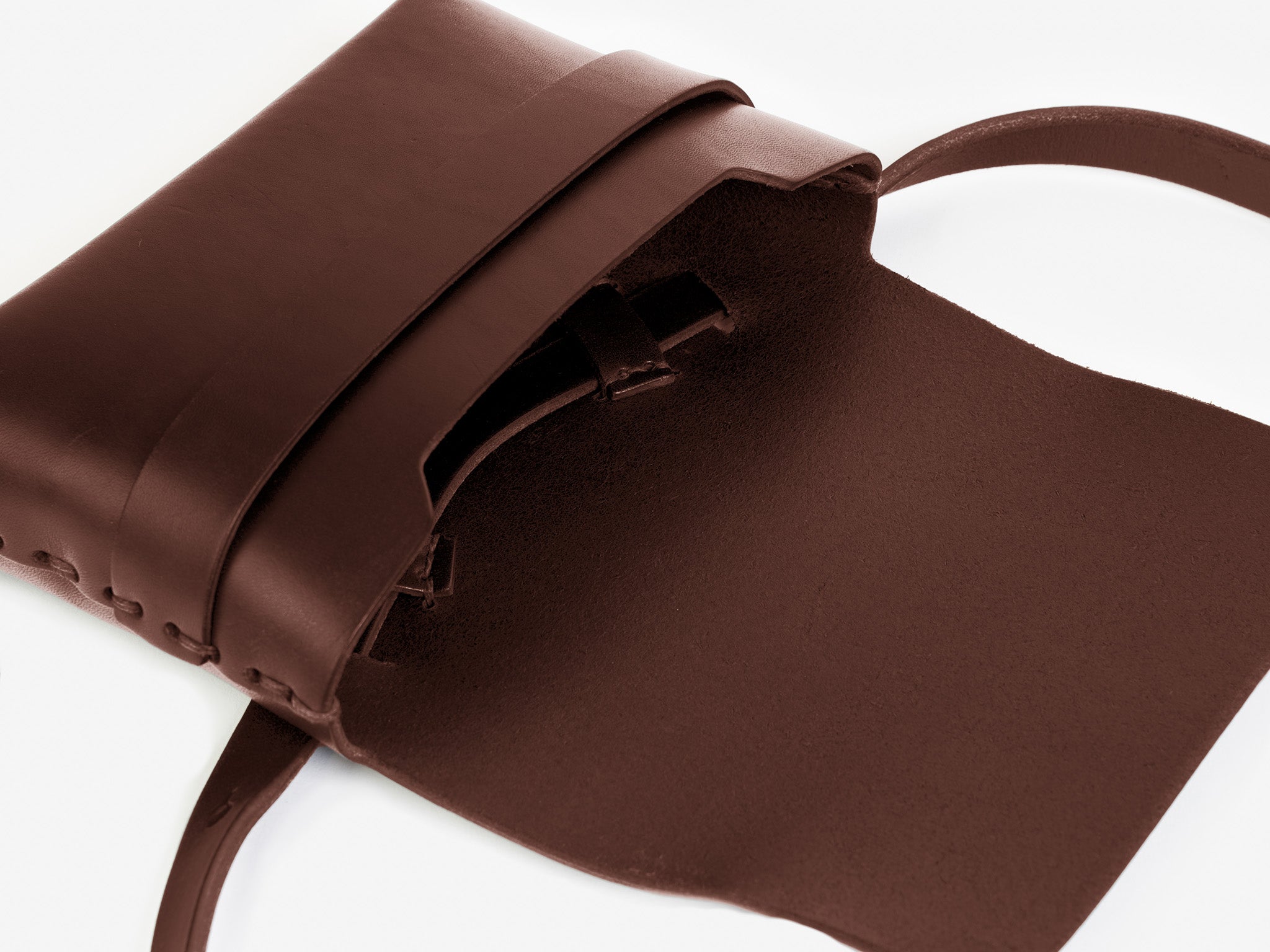 A hickory leather crossbody bag with a flap open, revealing some hand-stitched details. The bag has a strap and minimalist design, displayed on a white background.