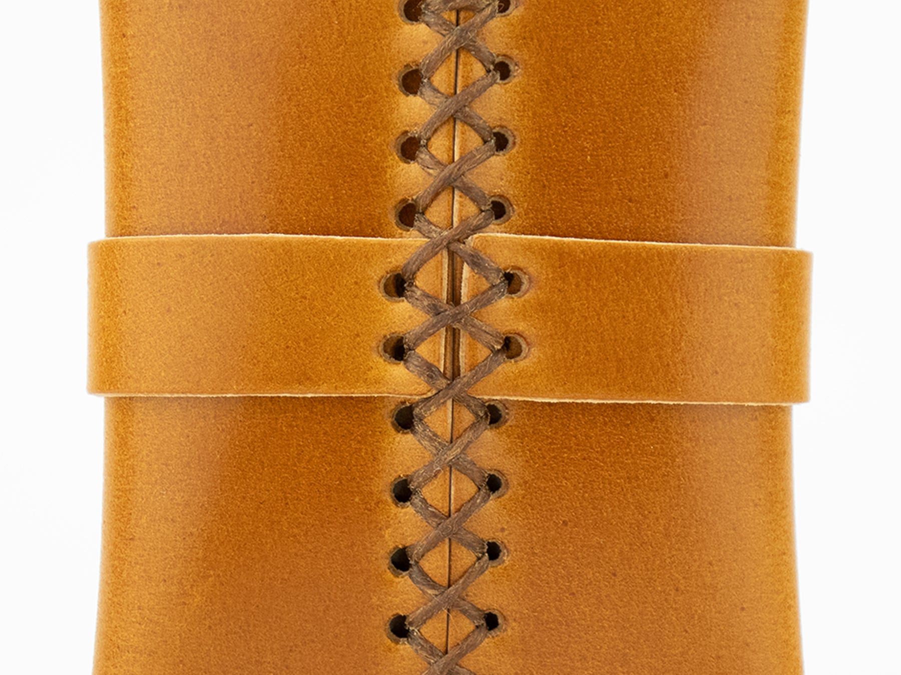 Close-up of tan leather with brown crisscross stitching and a horizontal leather strap across the center, showing detailed texture and craftsmanship.