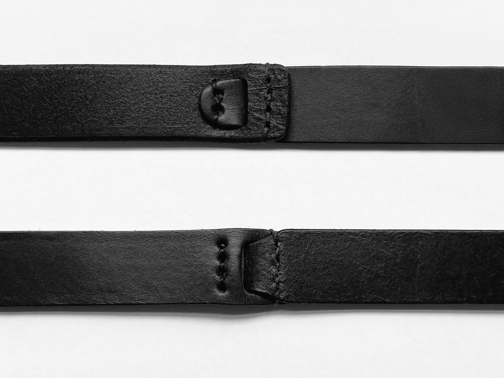 Two black leather belt straps are shown horizontally on a white background. Each strap has visible stitching and punched holes near the end.
