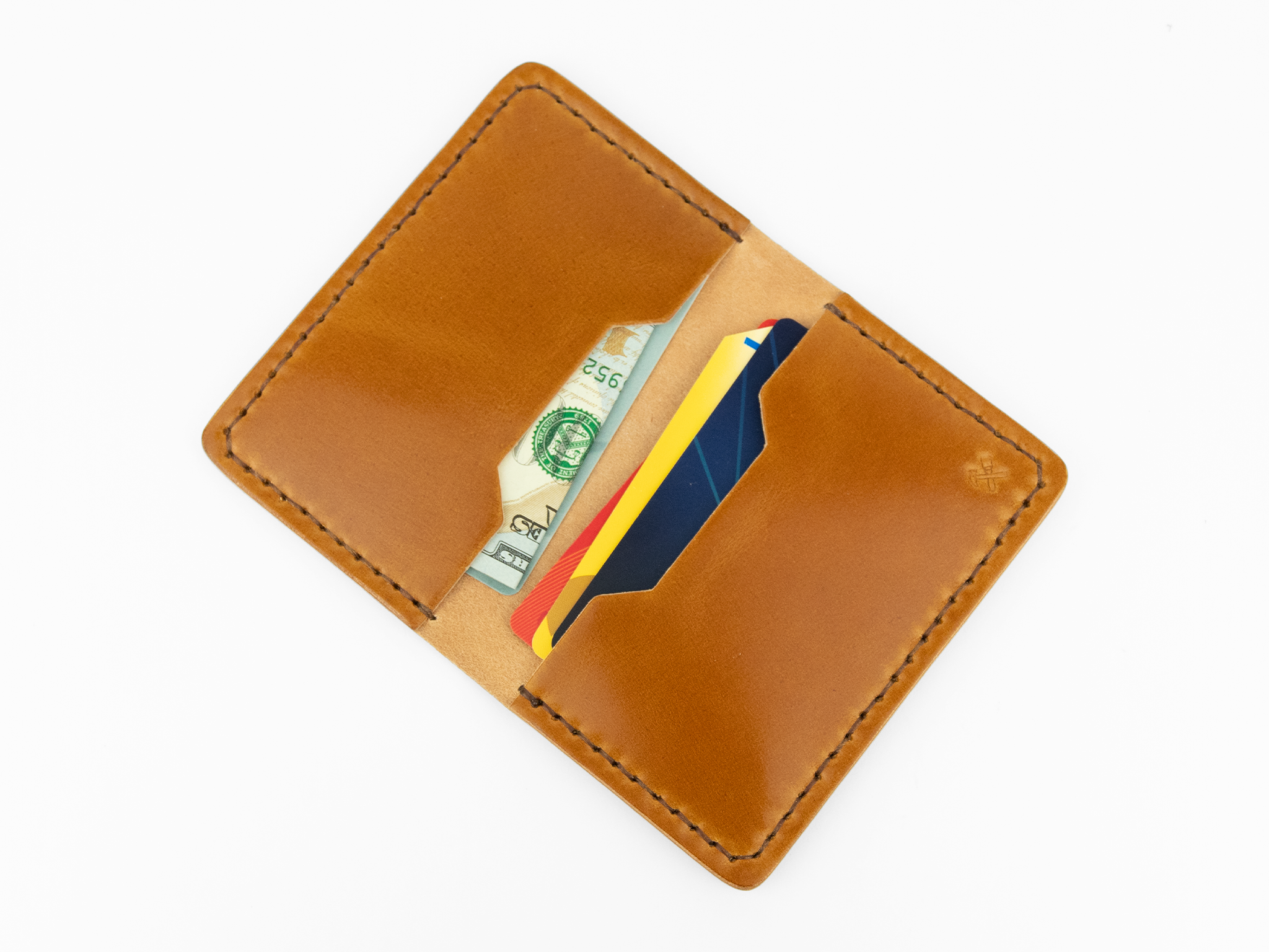 A tan cordovan leather wallet open to reveal paper currency and two credit cards inside, photographed on a white background.