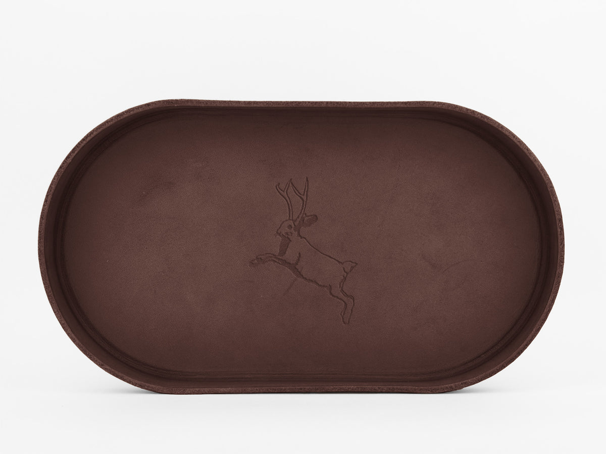 A brown, oval-shaped tray with a subtle engraved outline of a leaping animal, possibly a deer or antelope, centered on its surface. The background is plain white.

