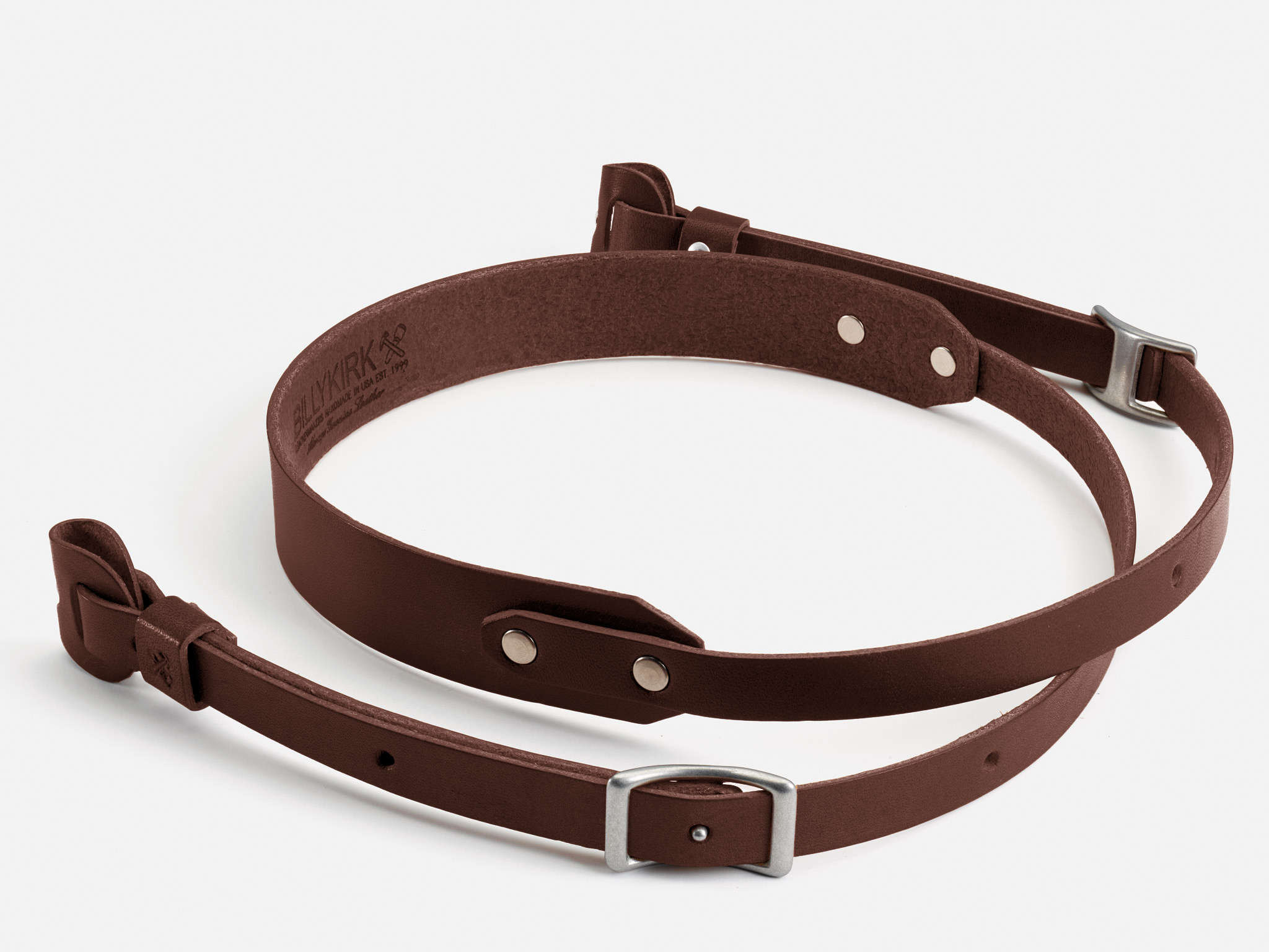 A brown leather rifle sling with silver metal buckles and rivets, displayed coiled on a white background.