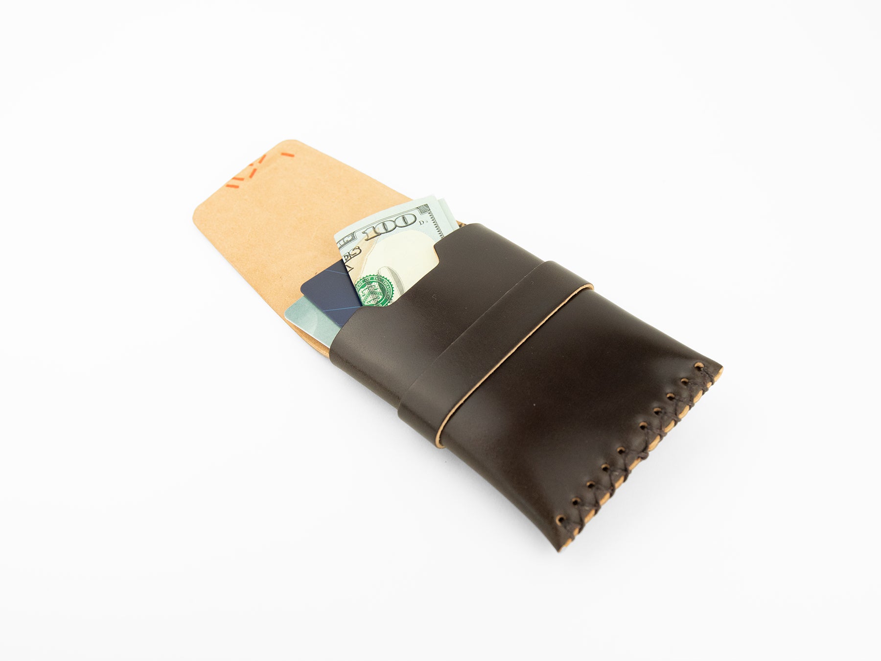 A brown leather wallet with visible stitching, partially open to reveal a $100 bill and two credit cards inside, placed on a white background.
