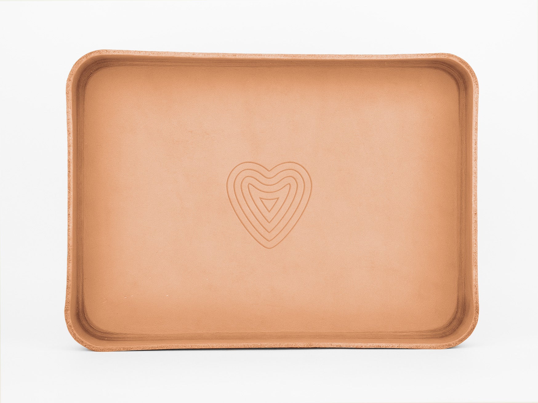 A rectangular tan leather tray with raised edges and a subtle, concentric heart design embossed in the center, set against a white background.