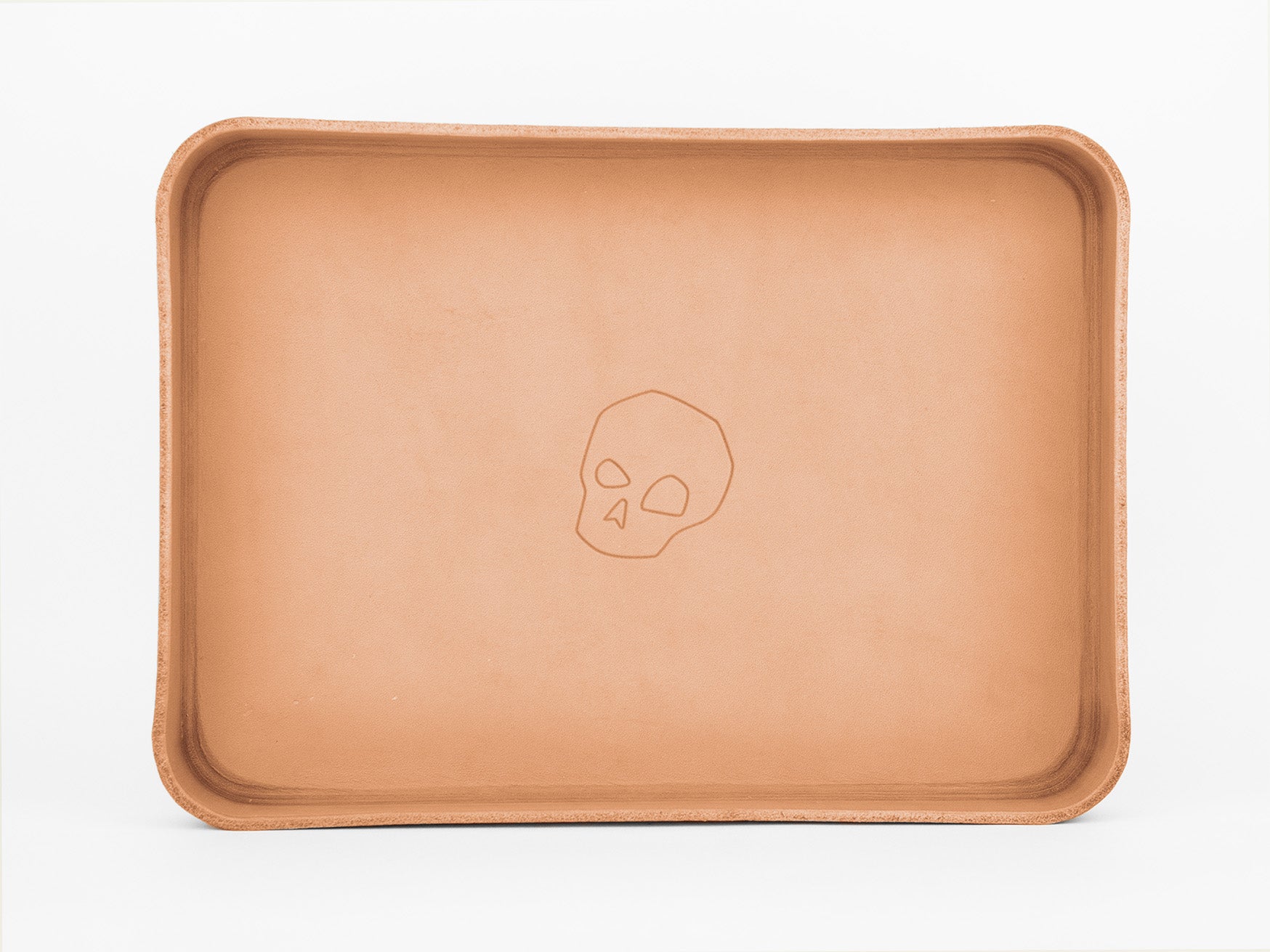A rectangular, tan leather tray with rounded edges. The tray features a simple, embossed skull design in the center. The background is plain white.
