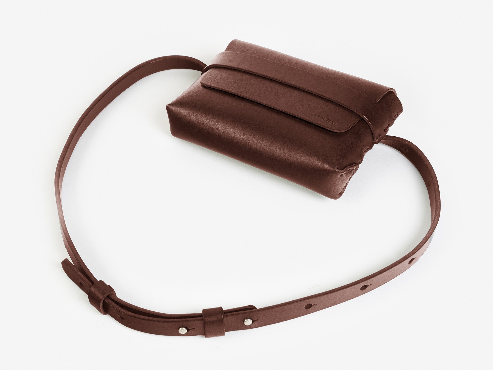 A hickory leather belt crossbody bag with a smooth finish, featuring a flap closure, subtle embossed branding, and an adjustable strap with silver-tone collar buttons, displayed against a white background.