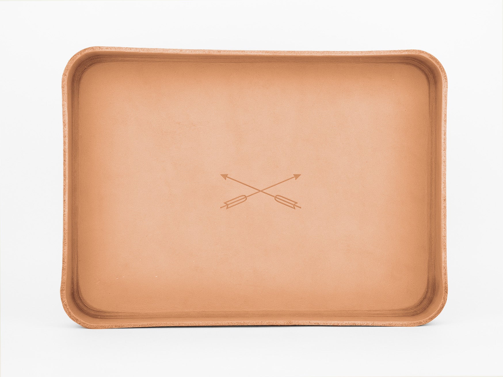 A rectangular tan leather tray with raised edges features two crossed arrows engraved in the center. The background is plain white.