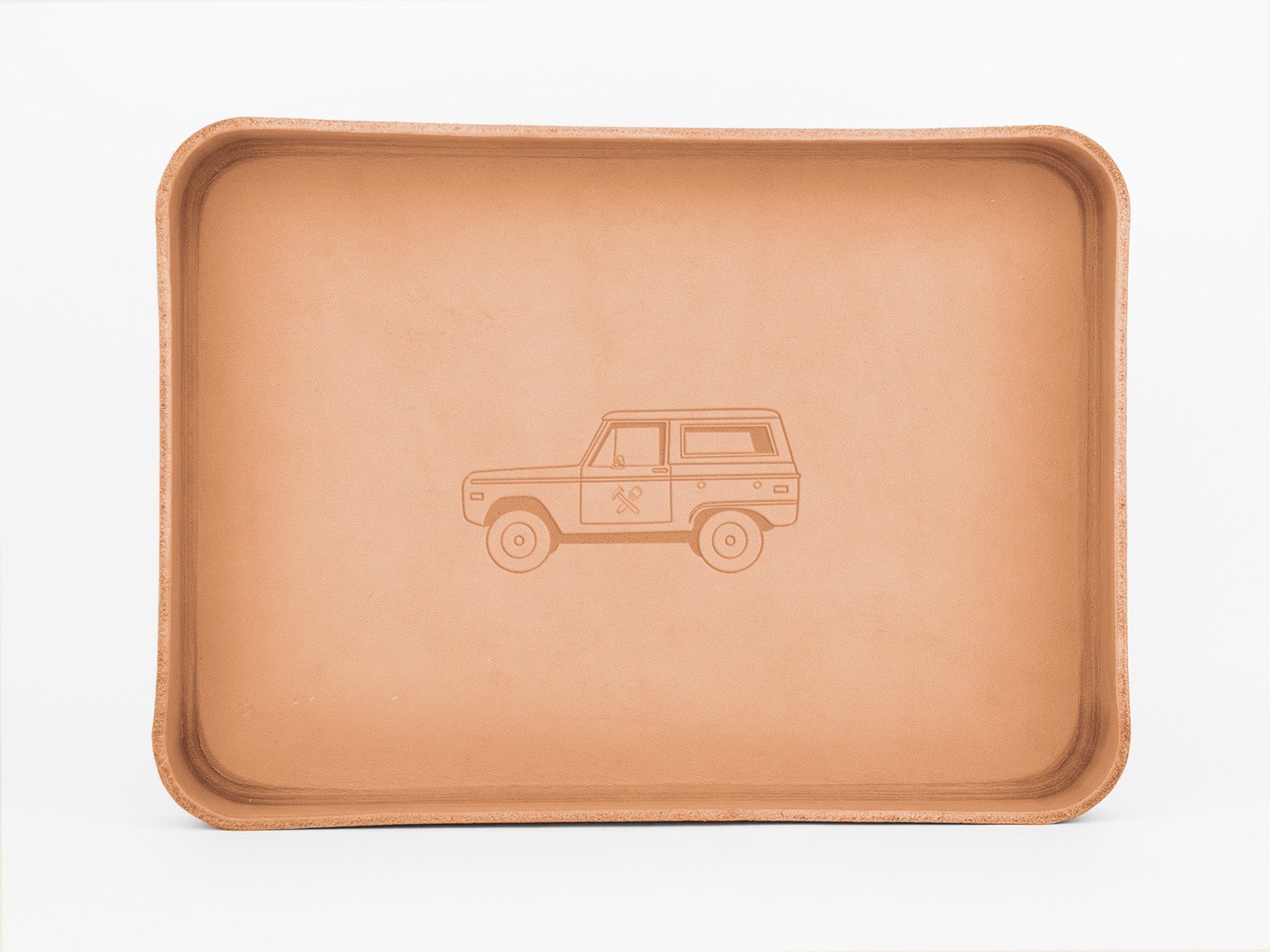 A rectangular, tan leather tray with rounded edges features an embossed illustration of a classic SUV on its flat surface. The background is white.