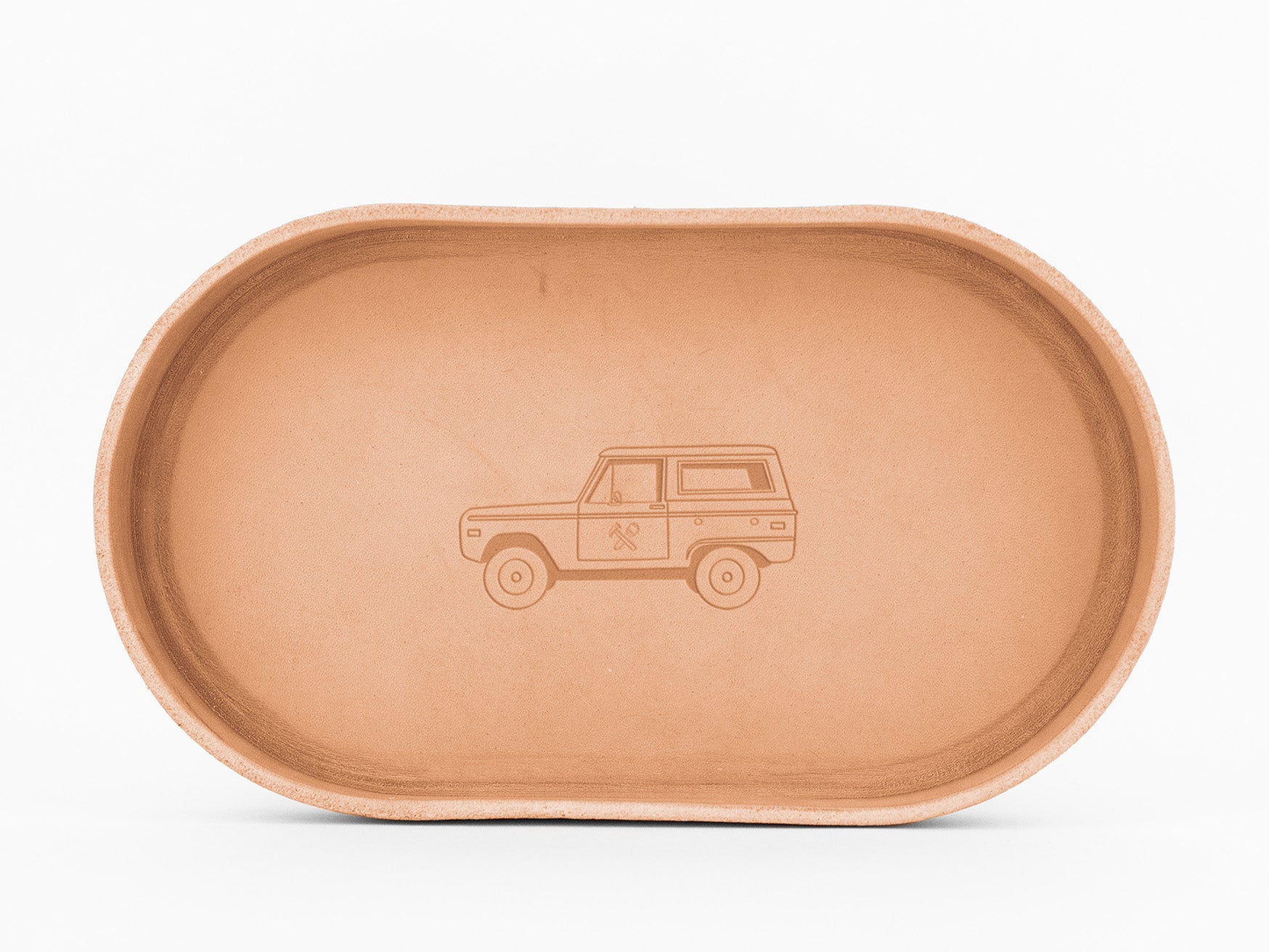 A shallow, oval-shaped, natural colored leather tray featuring a simple etched illustration of a vintage SUV truck in the center.