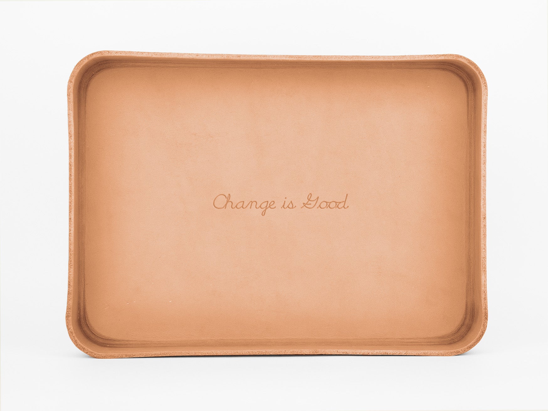 A rectangular, light brown leather tray with rounded corners. The phrase “Change is Good” is engraved in cursive text in the center of the tray. The background is plain white.