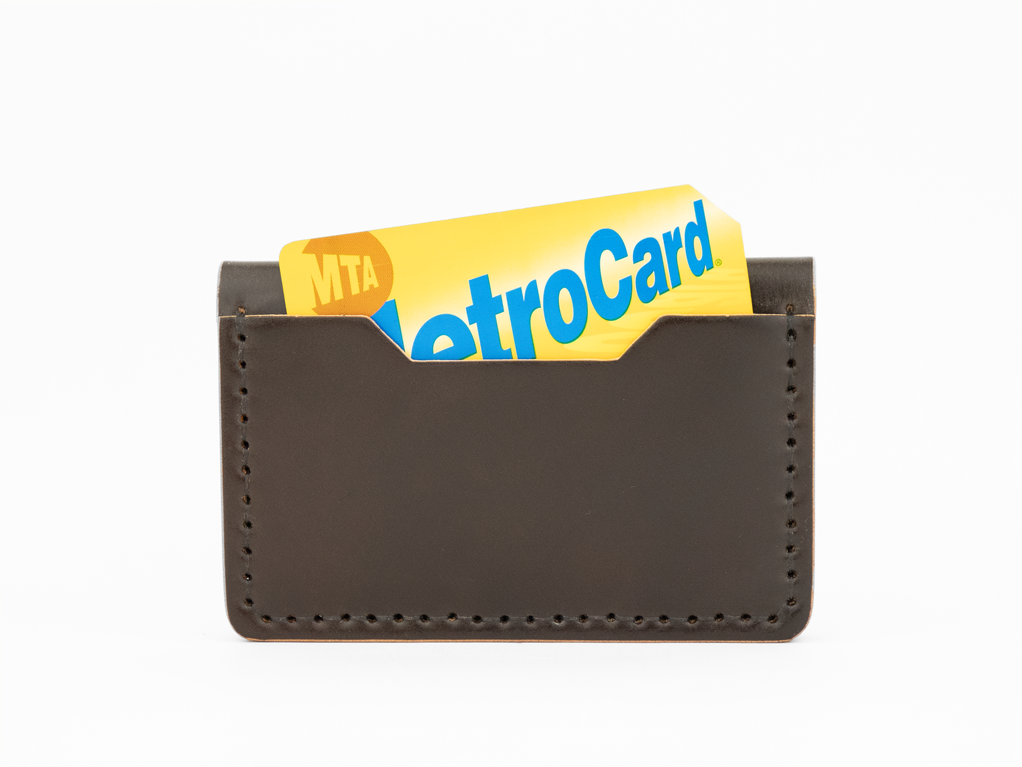 A dark brown cordovan leather card holder with visible stitching holds a yellow and blue MTA MetroCard, partially sticking out from the top.