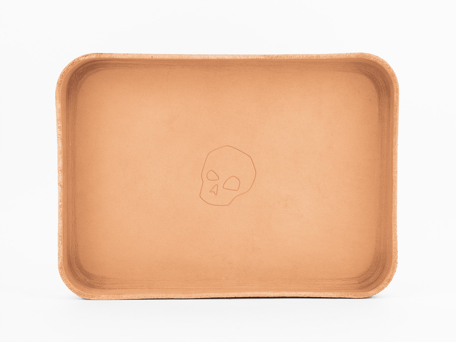 A rectangular, tan leather tray with rounded corners, featuring a simple outline of a skull engraved in the center. The background is plain white.