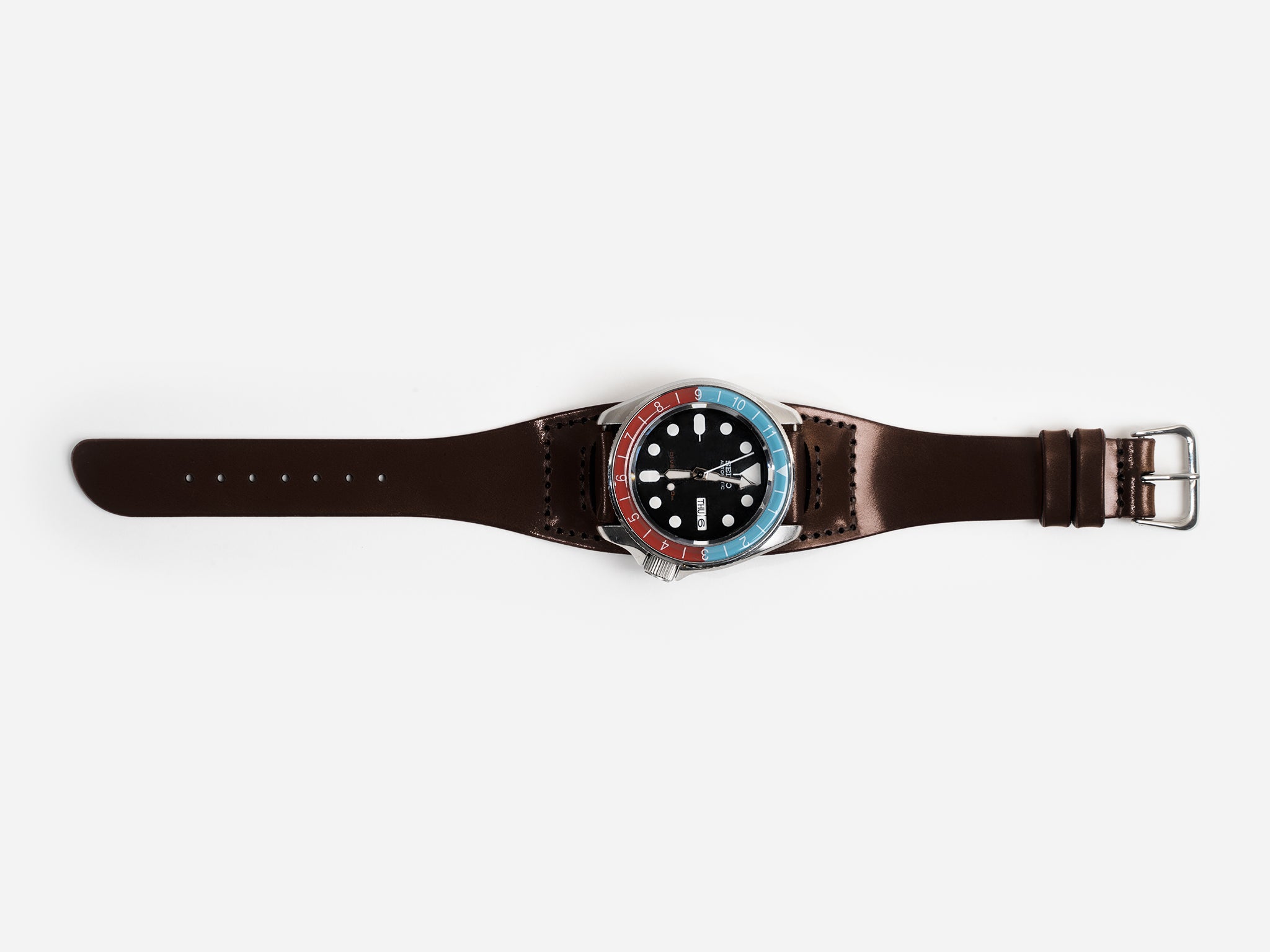 A dark brown cordovan leather watch strap with a round watch face featuring a blue and red bezel, white hour markers, and silver hands, displayed on a white background.