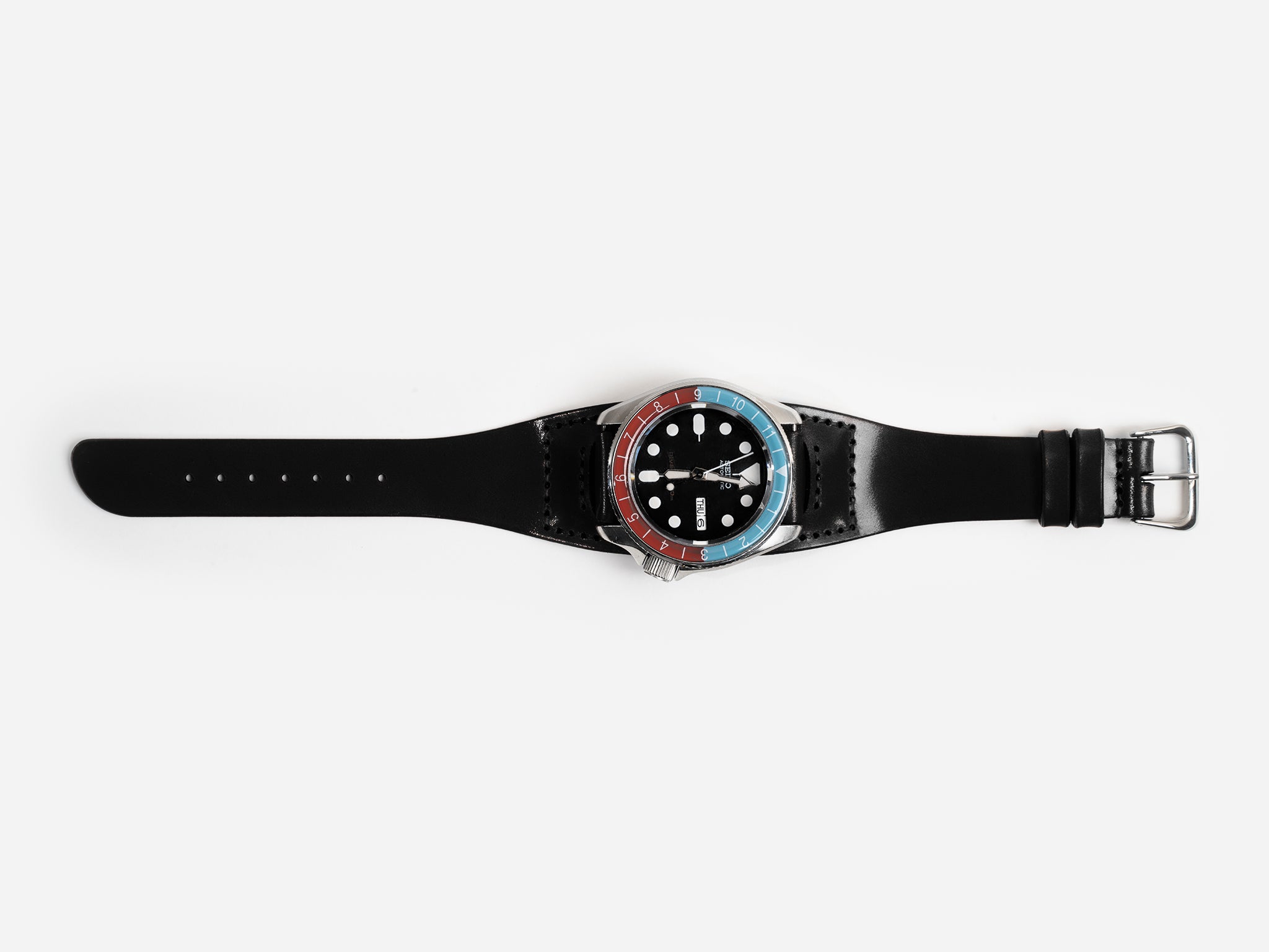 A black cordovan leather watch strap with a round watch face featuring a blue and red bezel, white hour markers, and silver hands, displayed on a white background.