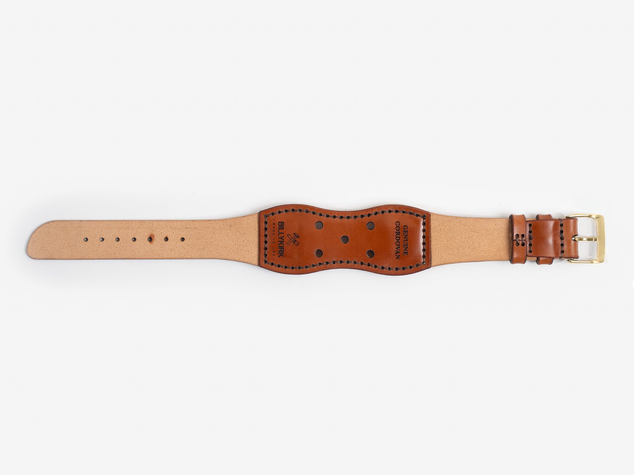 The back of a tan cordovan leather watch strap with a brass buckle lies flat on a white background; it has black thread stitched edges and an hourglass shape.