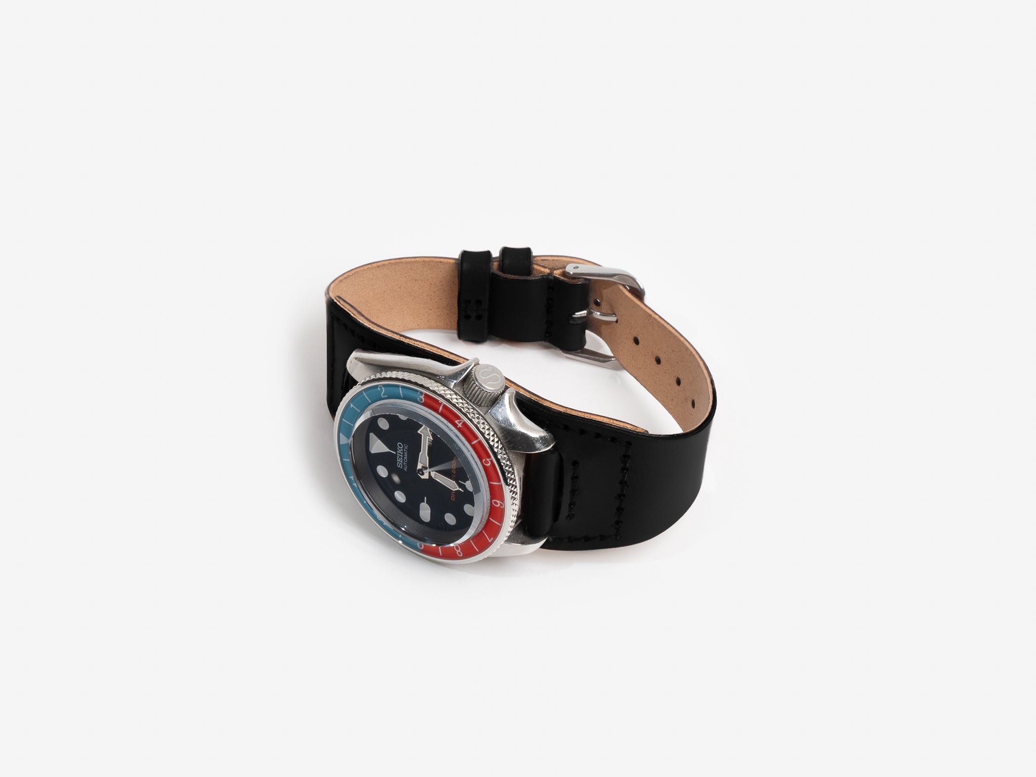 A Seiko watch face with a black cordovan leather strap and a red and blue bezel, displayed on a white background. The watch face features large hour markers and silver hands.