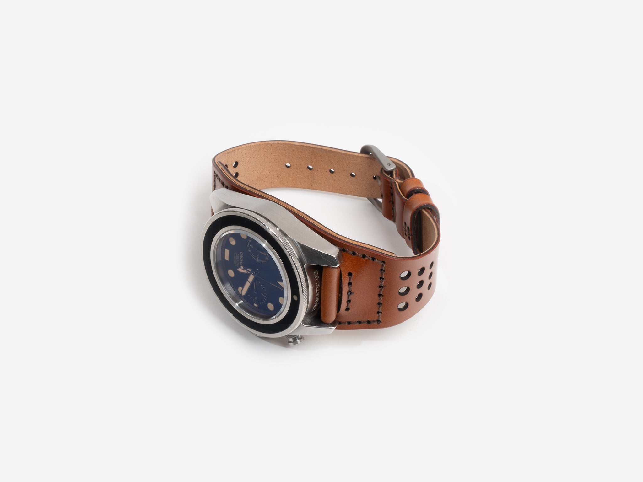 A fastened tan cordovan leather watch strap, silver buckle, and a round black dial featuring multiple subdials and gold accents, displayed flat on a white background.
