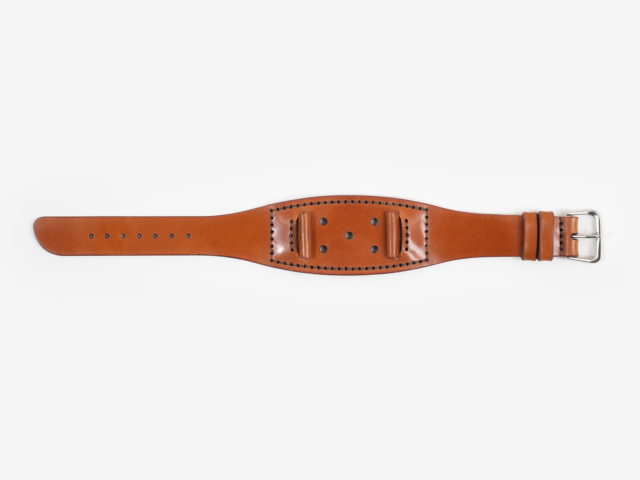 A tan cordovan leather watch strap with a silver buckle lies flat on a white background; it has stitched edges and multiple holes for adjustment.