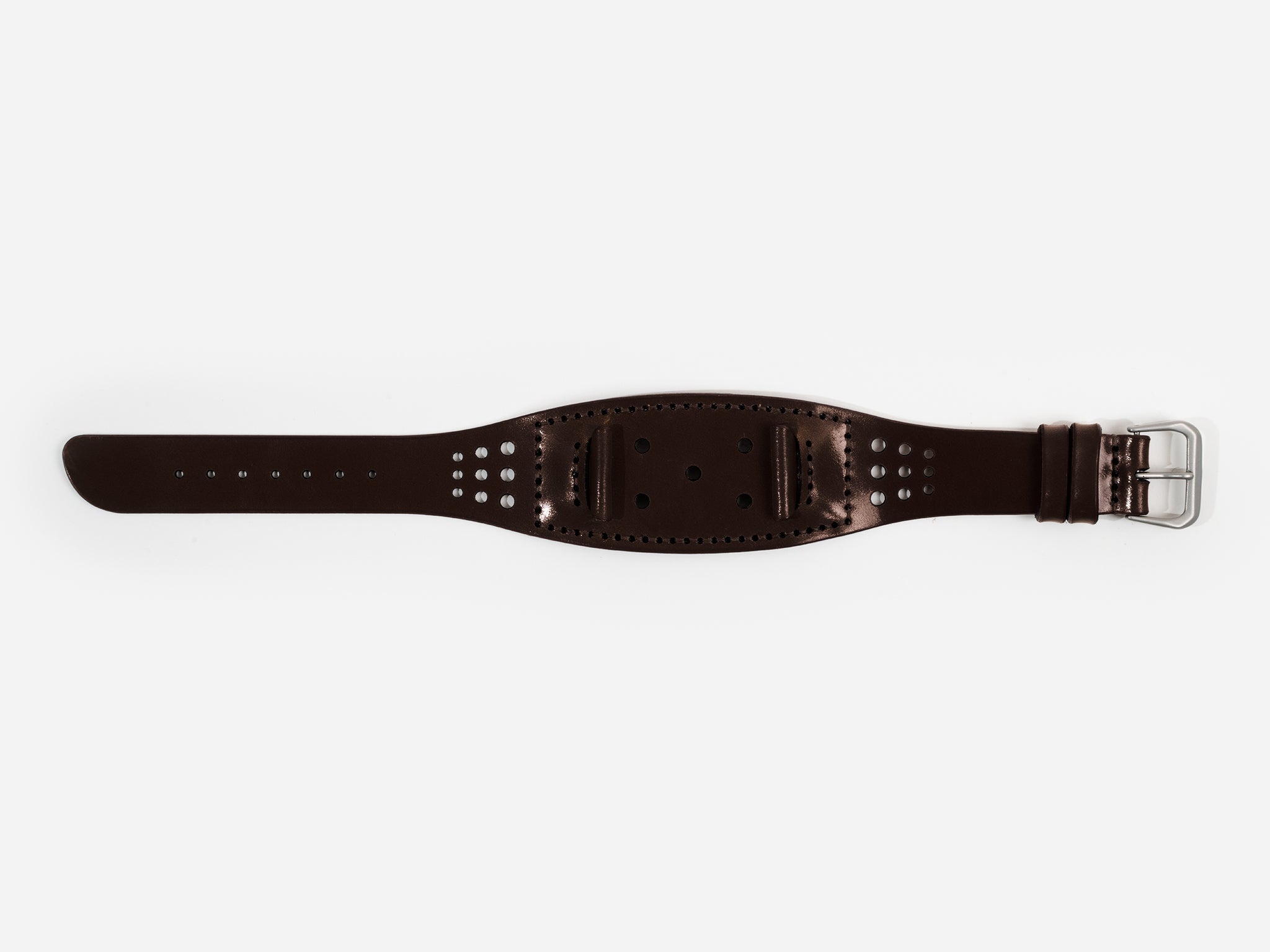 A dark brown cordovan leather watch strap with a silver buckle lies flat on a white background; it has stitched edges and multiple holes for adjustment.