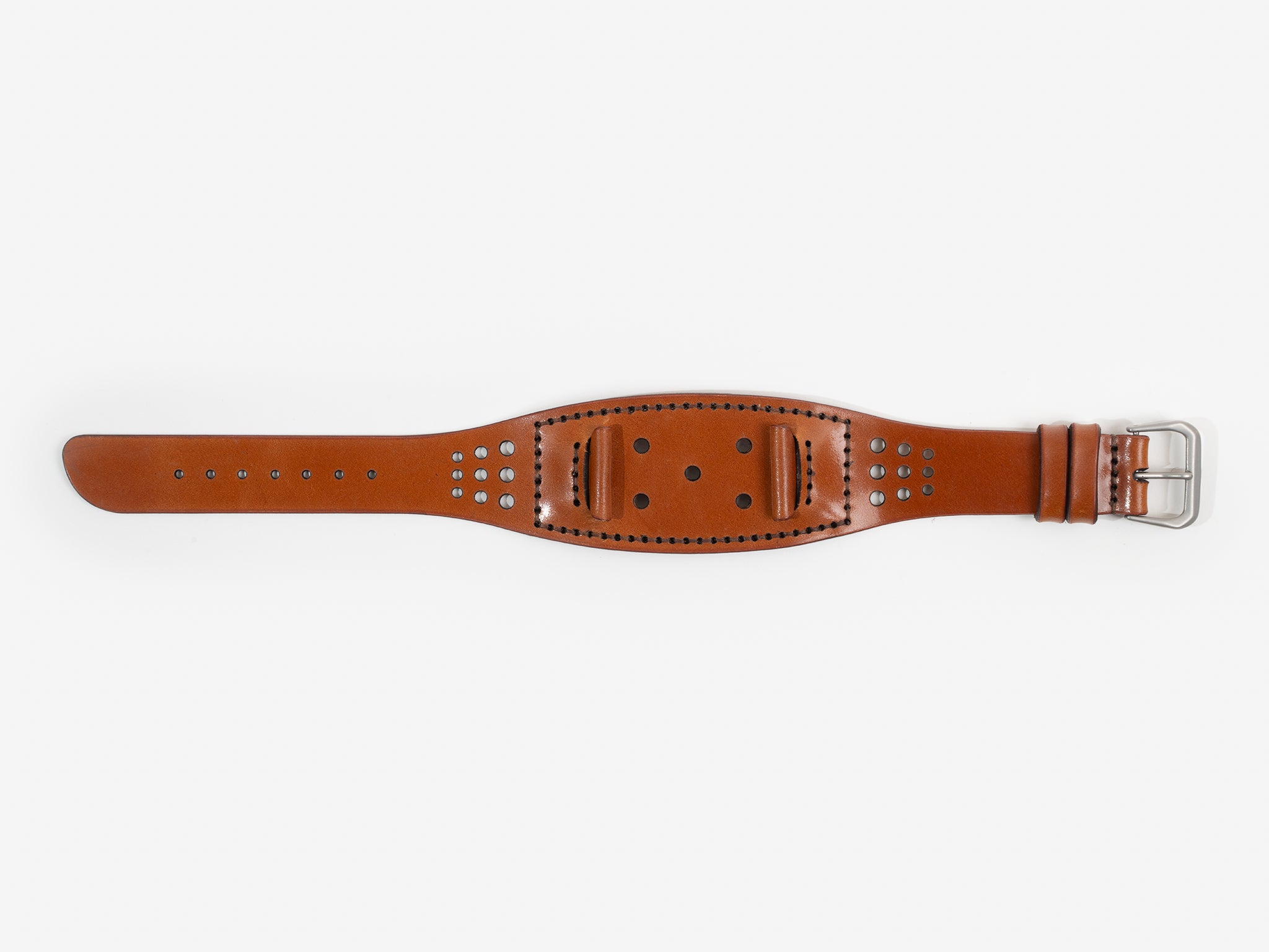 A tan cordovan leather watch strap with a silver buckle lies flat on a white background; it has stitched edges and multiple holes for adjustment.