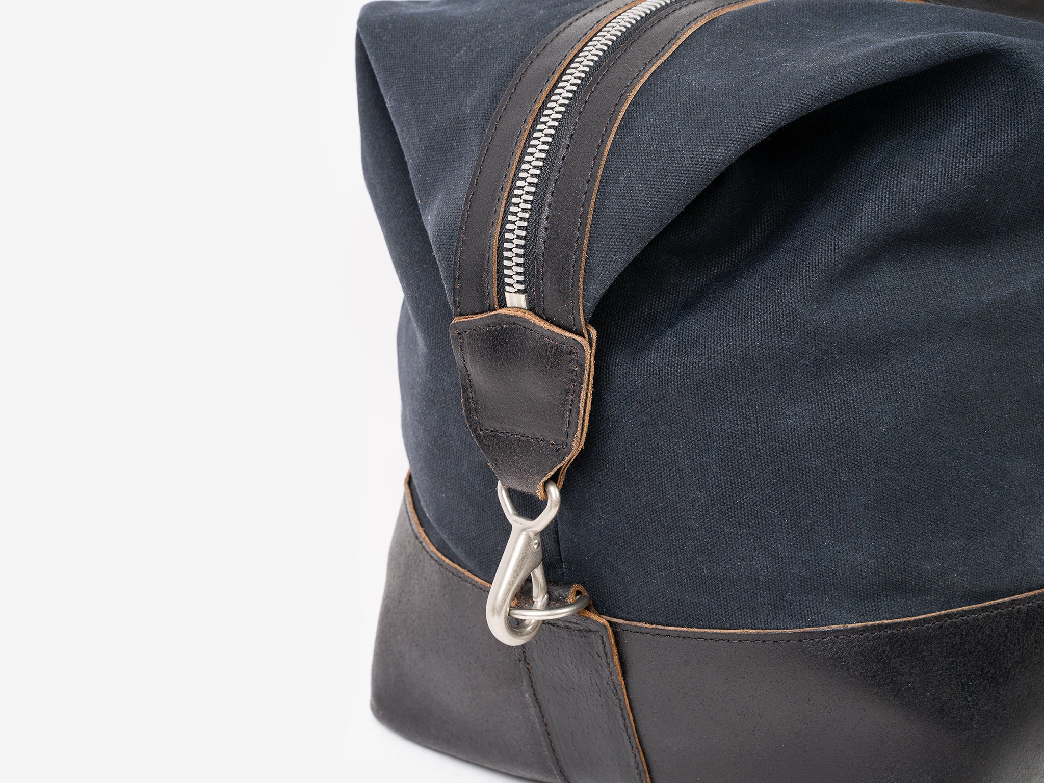 Close-up of a navy blue and black fabric bag with brown stitching, featuring a silver zipper and clasp hook attached to a leather strap.