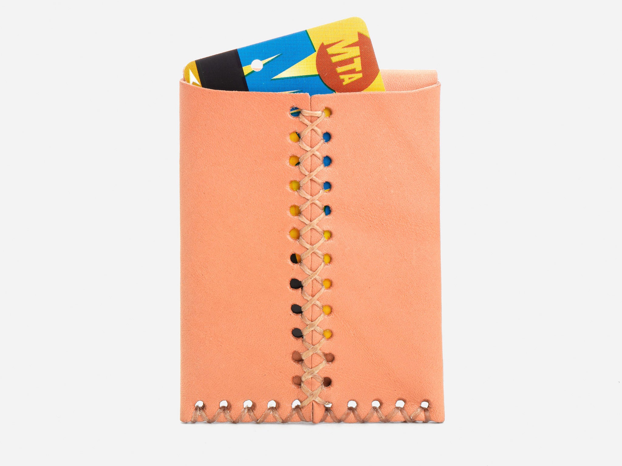 A tan leather cardholder with a central crisscross stitching pattern holds a partially visible MTA subway card against a white background.