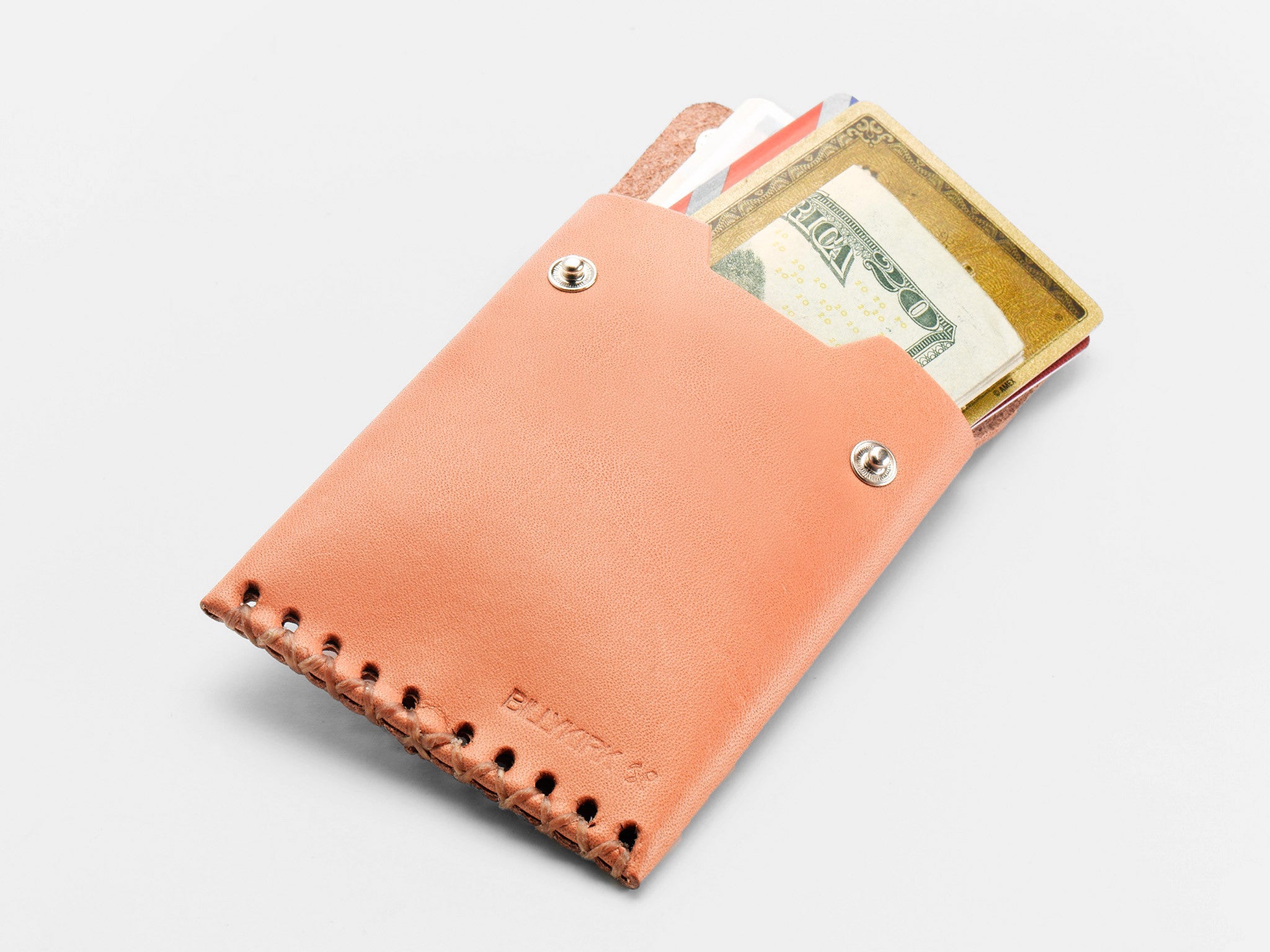 A tan leather wallet with visible stitching holds several credit cards and a folded U.S. twenty-dollar bill, partially sticking out from the top. The wallet is placed on a white surface.