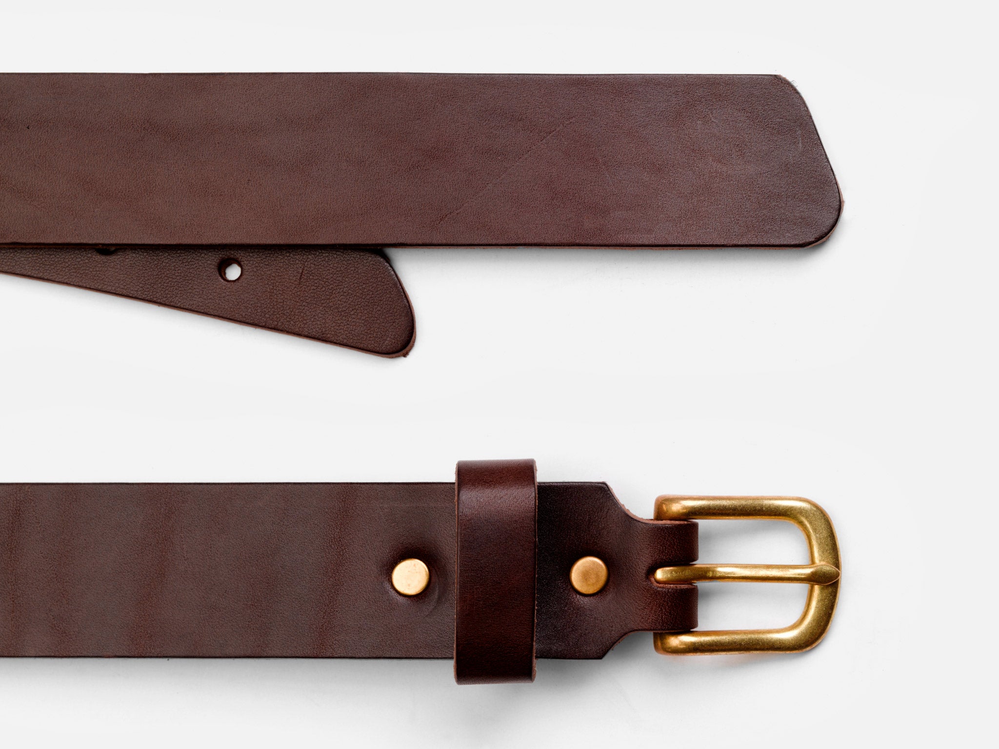 A close-up view of a brown leather belt with a gold buckle and metallic rivets, laid flat on a white surface. The belt’s end and buckle are both visible.