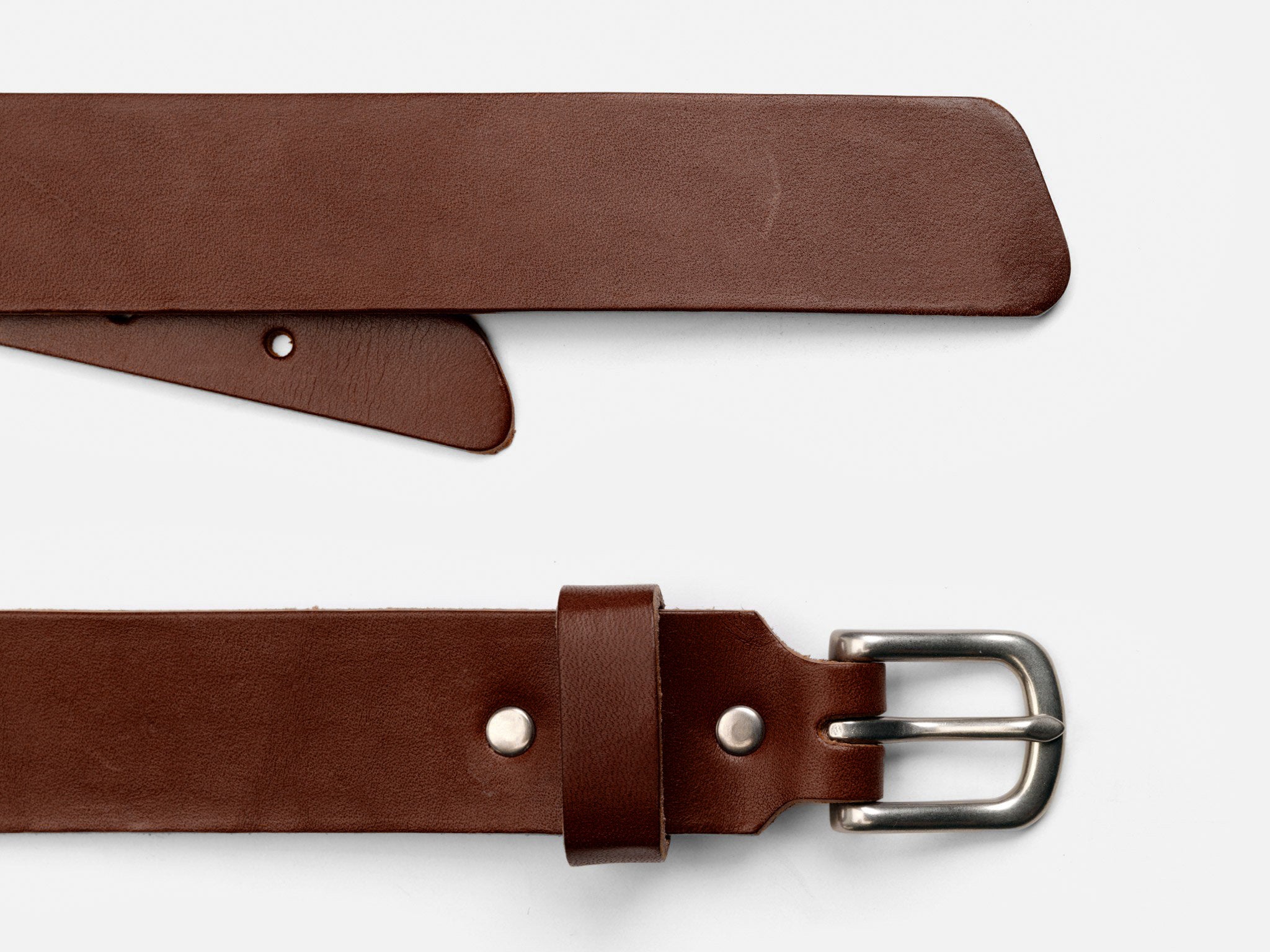 A brown leather belt with a silver buckle is shown laid flat on a white background. The belt is positioned to display both the pointed end and the buckle end with metal rivets.