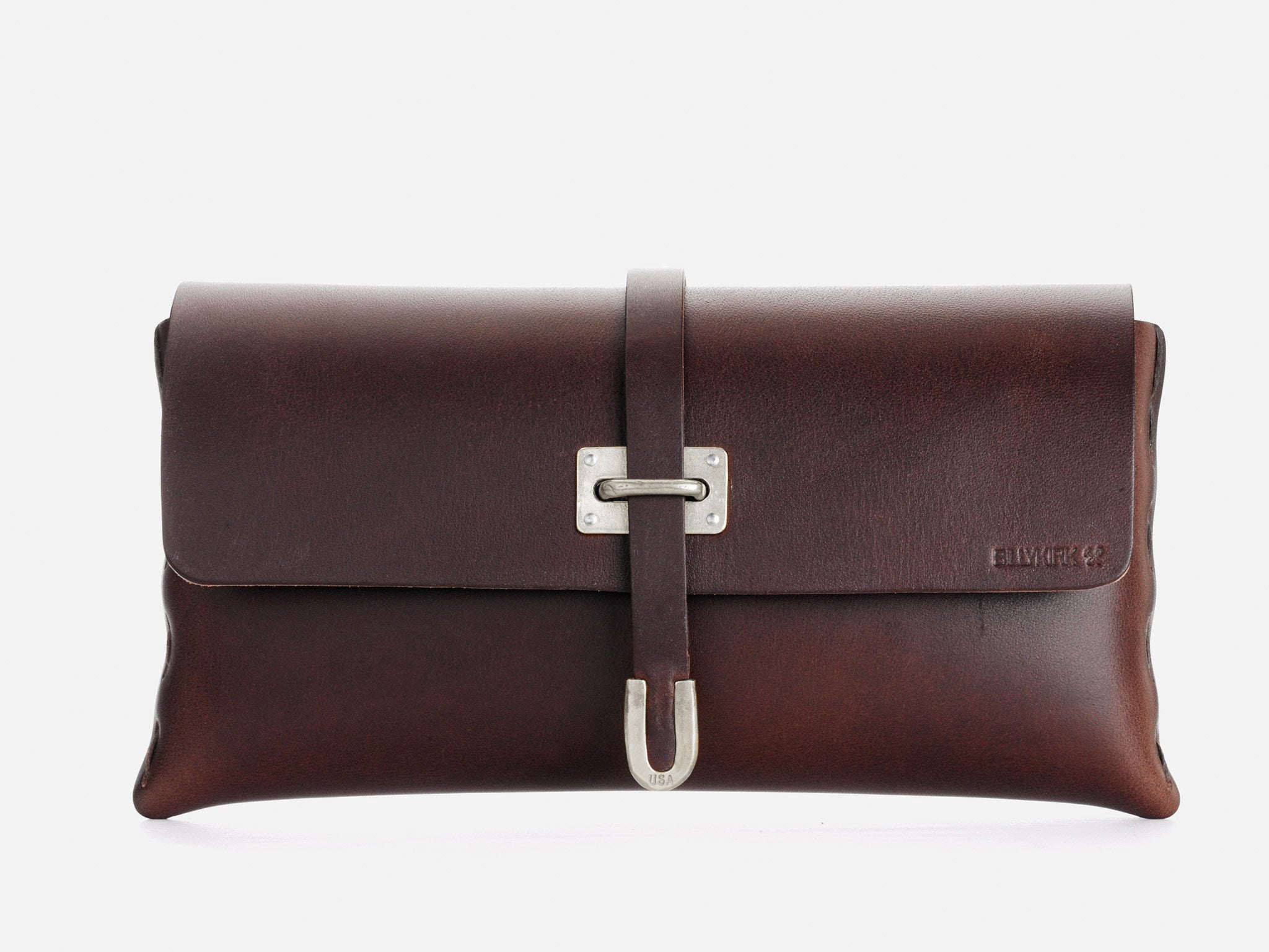 A dark brown leather clutch bag with a silver buckle clasp and a strap running vertically down the center. The brand name is embossed on the bottom right corner of the bag. The background is plain white.
