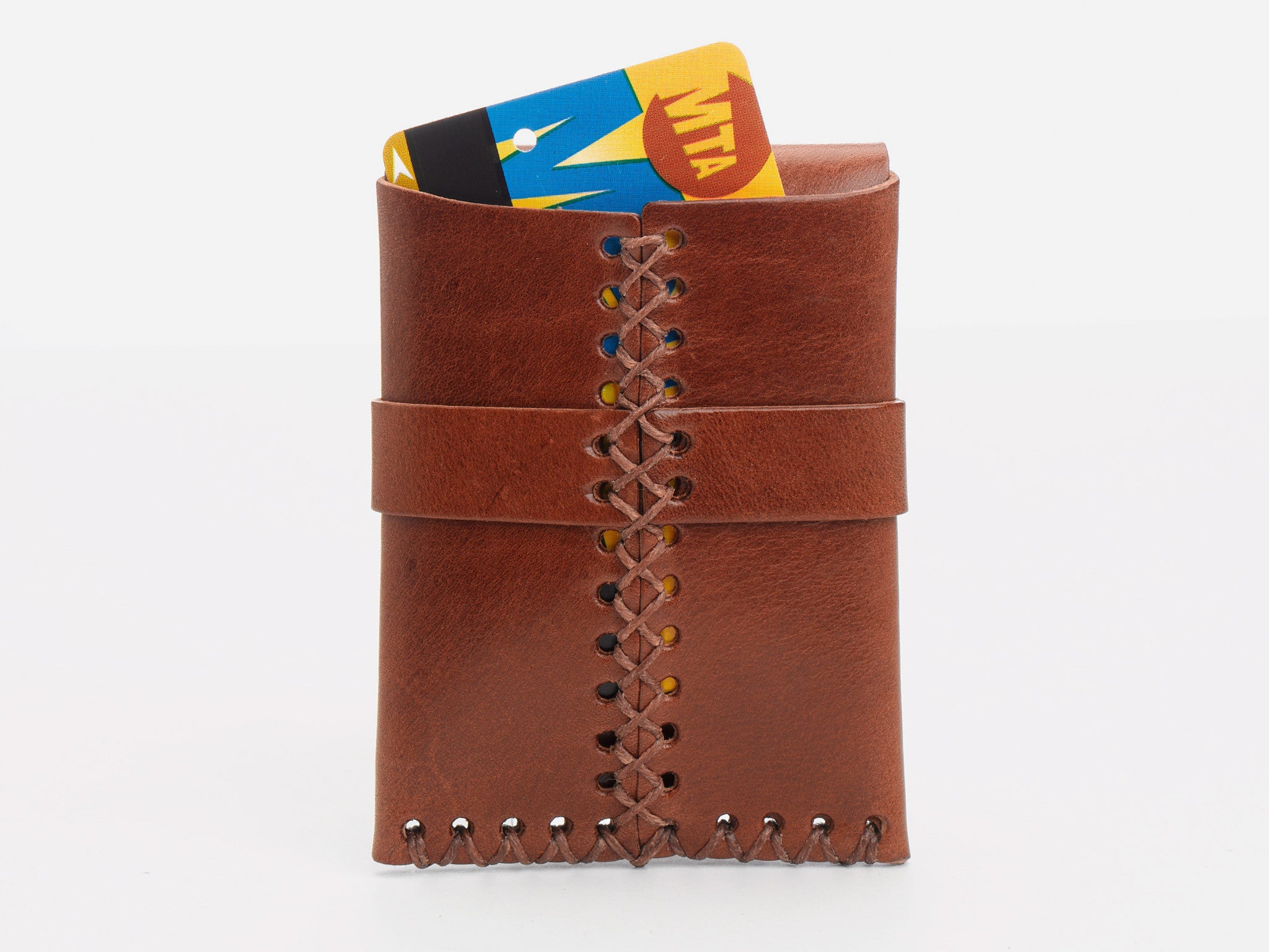 A tan leather wallet with visible stitching holds a New York City MetroCard,  partially sticking out of the rear wallet on a white background.