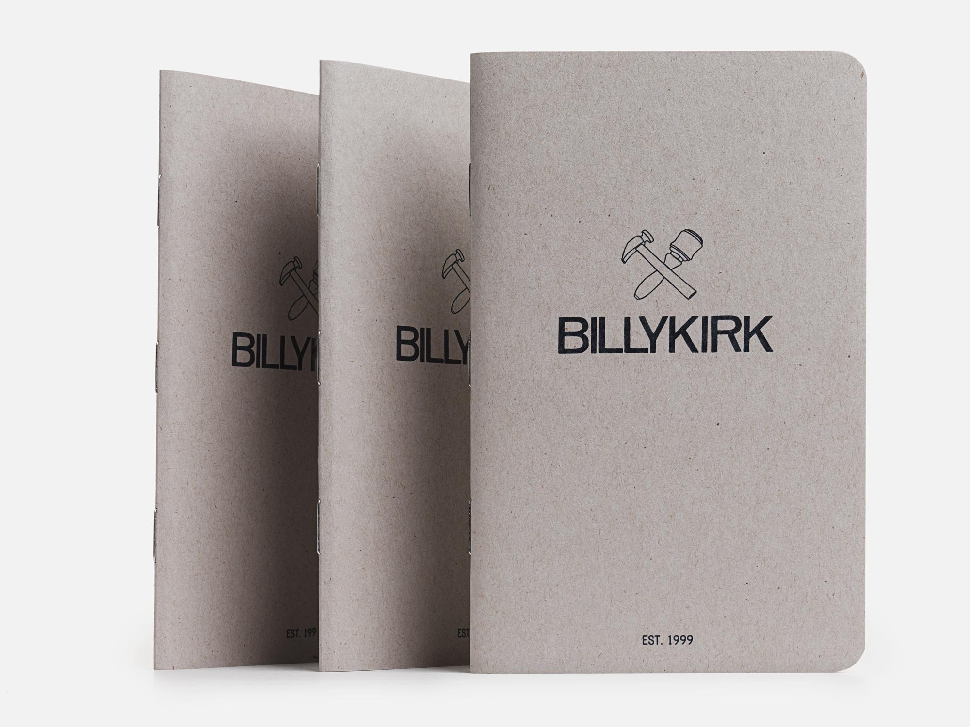 Three gray Billykirk notebooks stand upright in a row. Each has the Billykirk logo with a hammer and mallet above the brand name, and EST. 1999 printed at the bottom on a plain background.