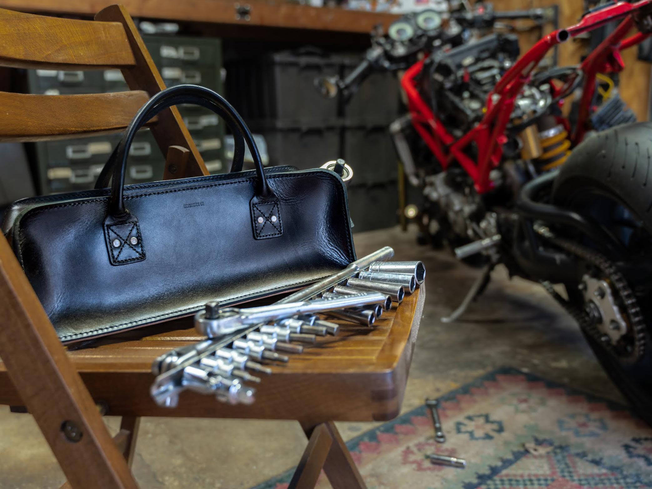 A black tool bag on a wooden chair with tools inside a motorcycle repair shop