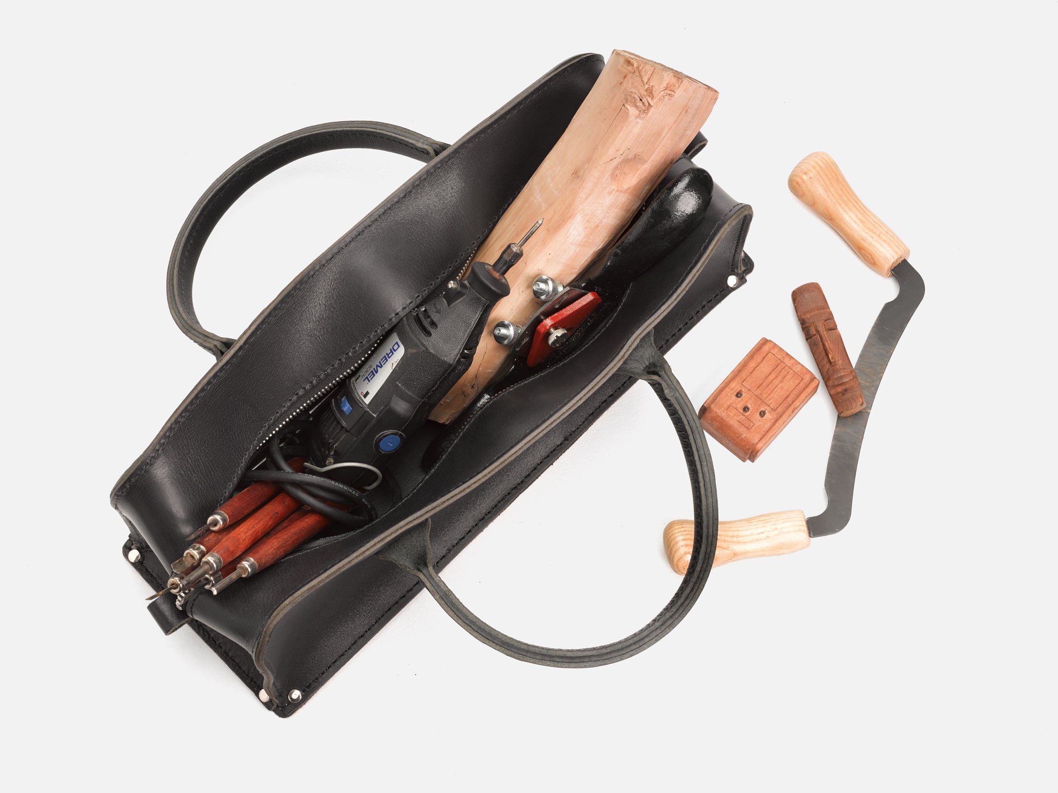 A top view of a black leather tool bag with rivet reinforced corners and a variety of tools in the bag set in a white background